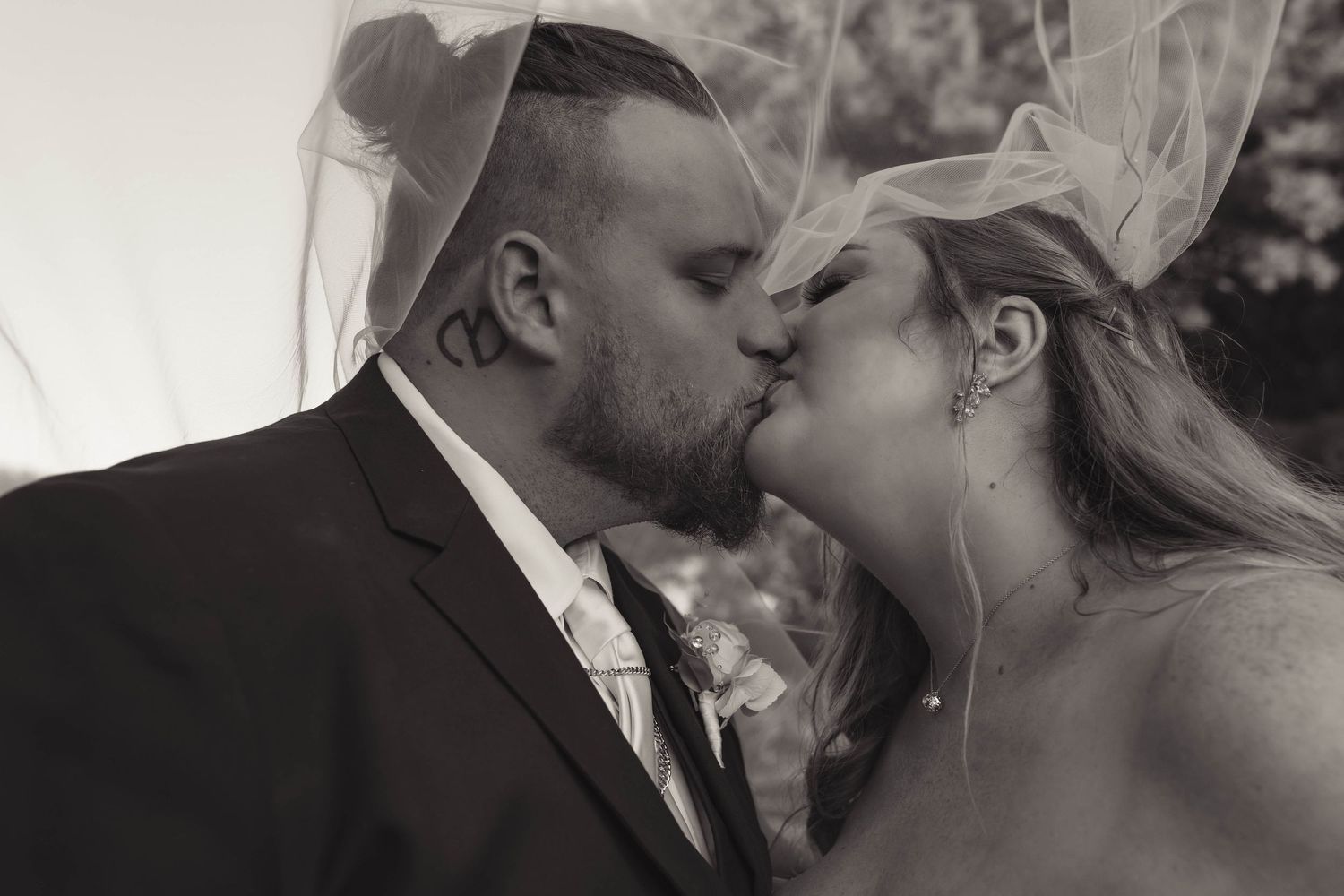 Black and white photo of bride and groom sharing a passionate kiss under a flowing veil.
