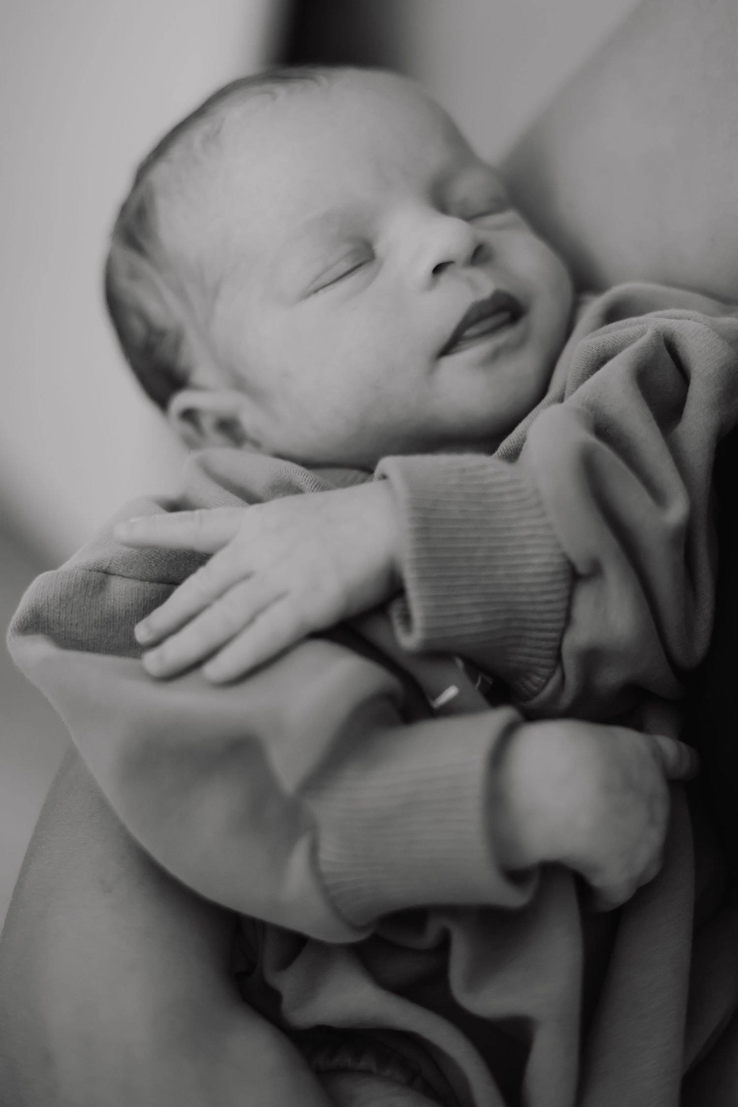 Black and white close-up photo of a sleeping newborn baby wrapped in a cozy sweater.