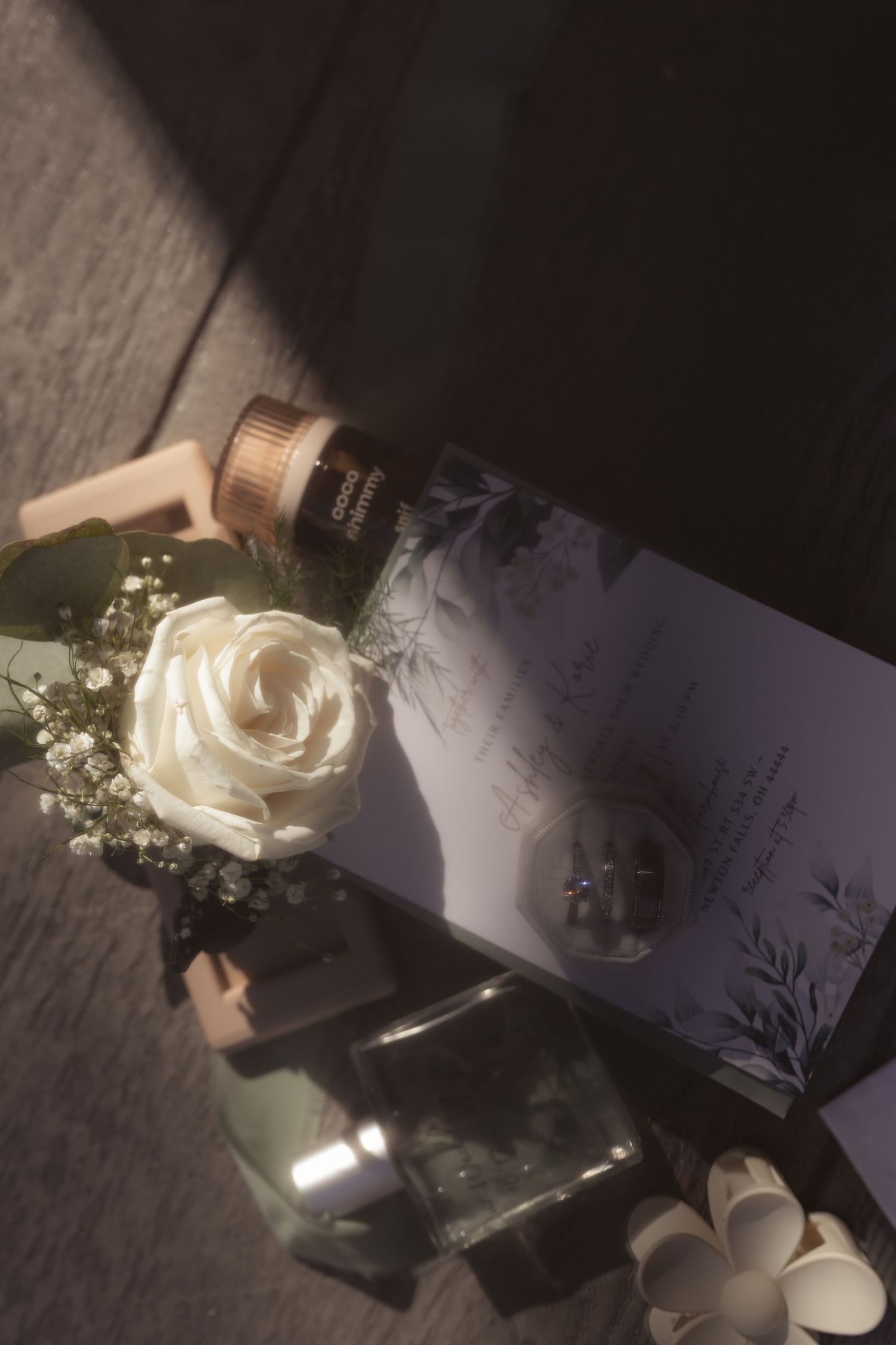 Elegant flat lay with white rose, luxury perfume bottle, and floral stationery in moody dark lighting.