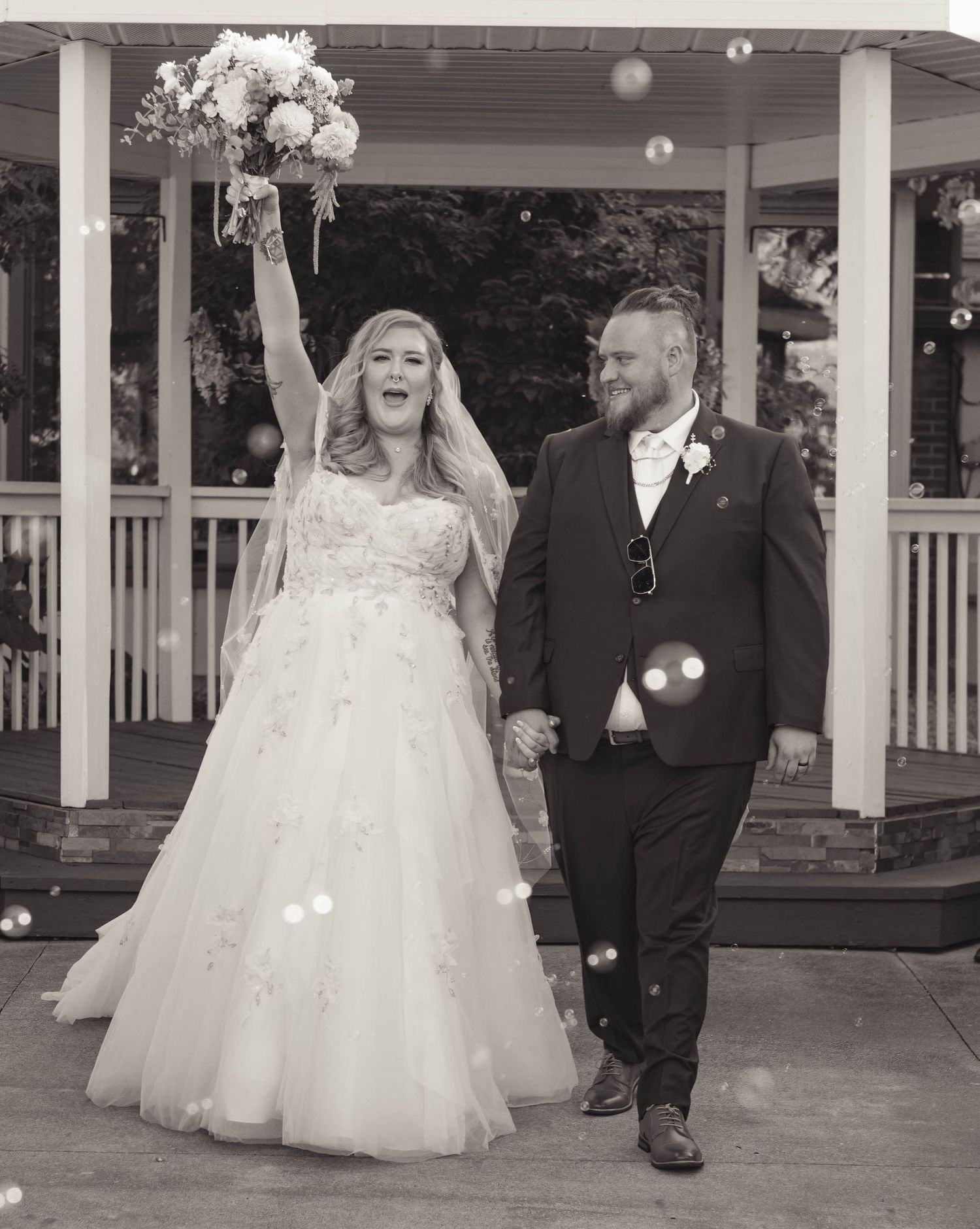 Black and white photo of a joyful bride and groom exiting their wedding ceremony with bubbles floating around them.