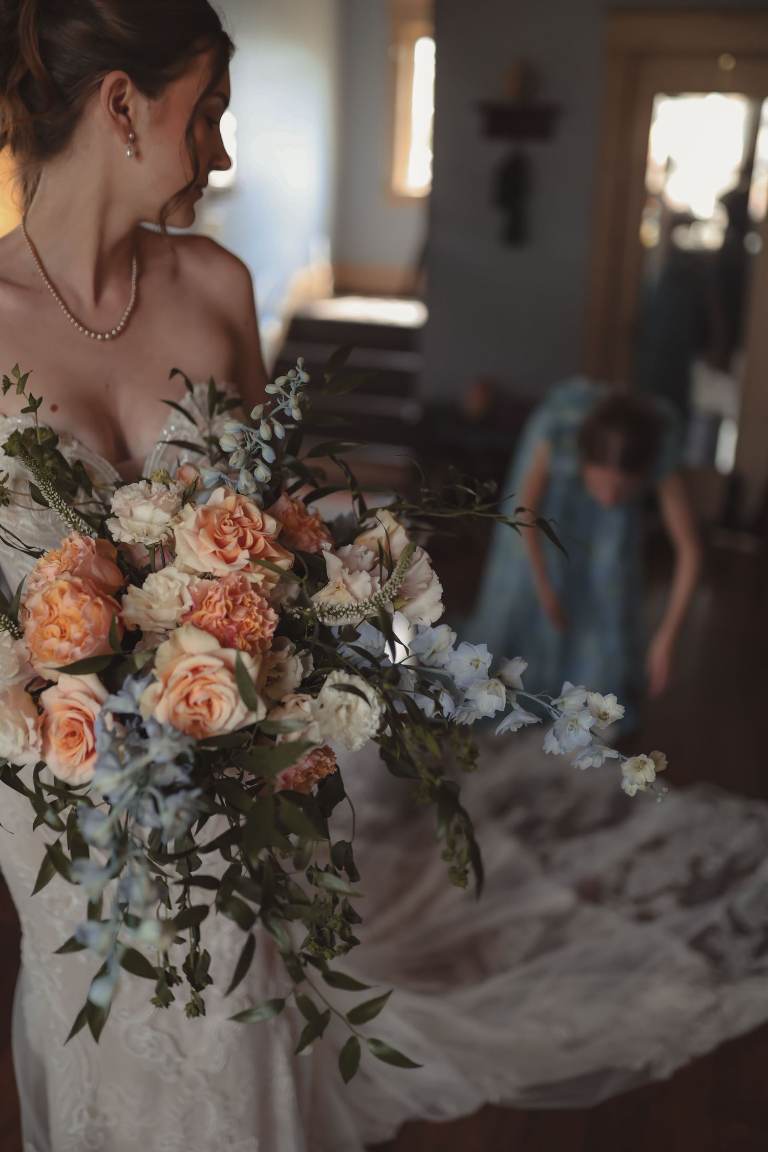 Bride holds lush bridal bouquet of peach roses and white blooms in soft indoor lighting.