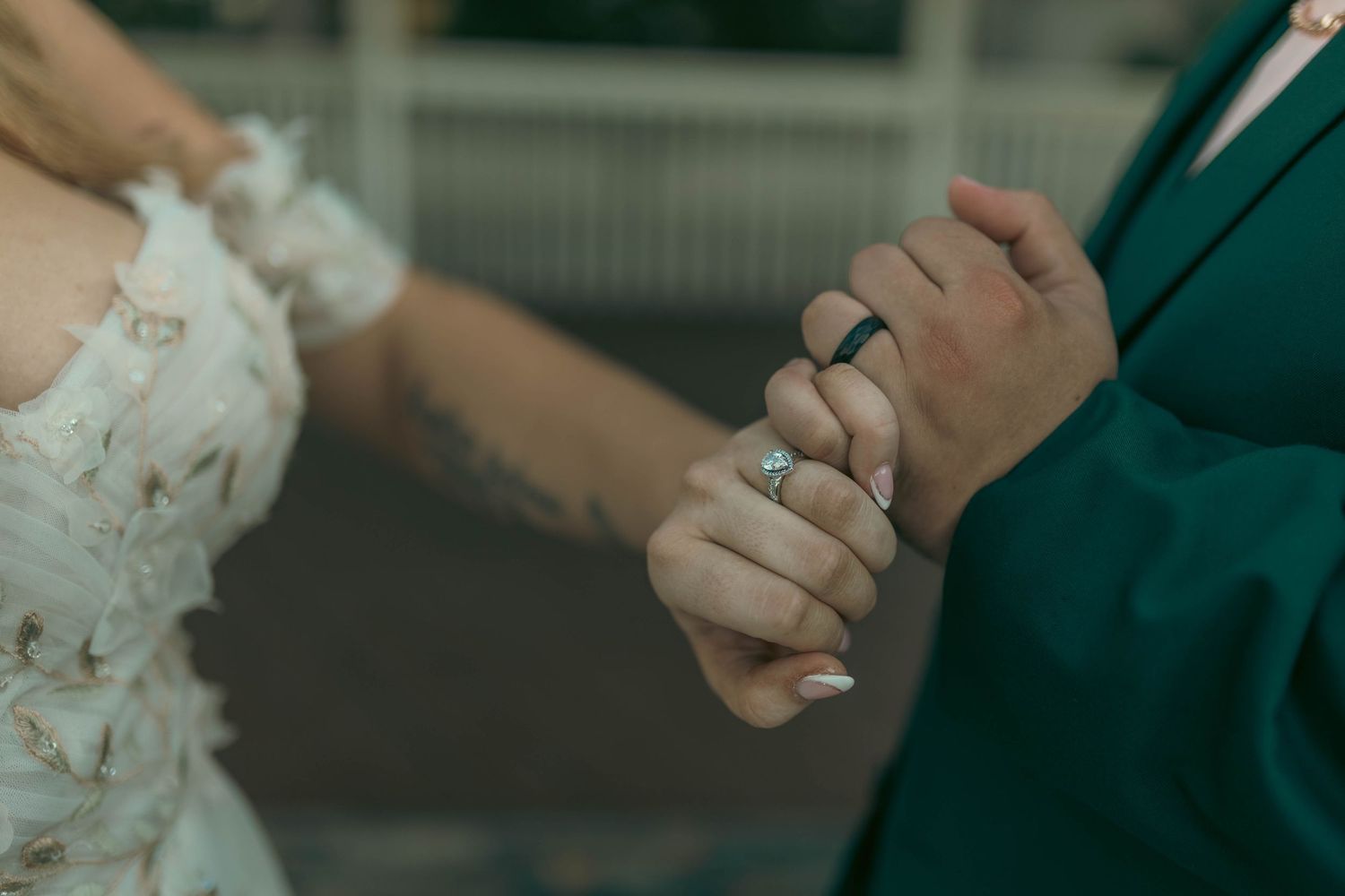 Close-up of a bride and groom holding hands, showcasing a diamond engagement ring and wedding bands.