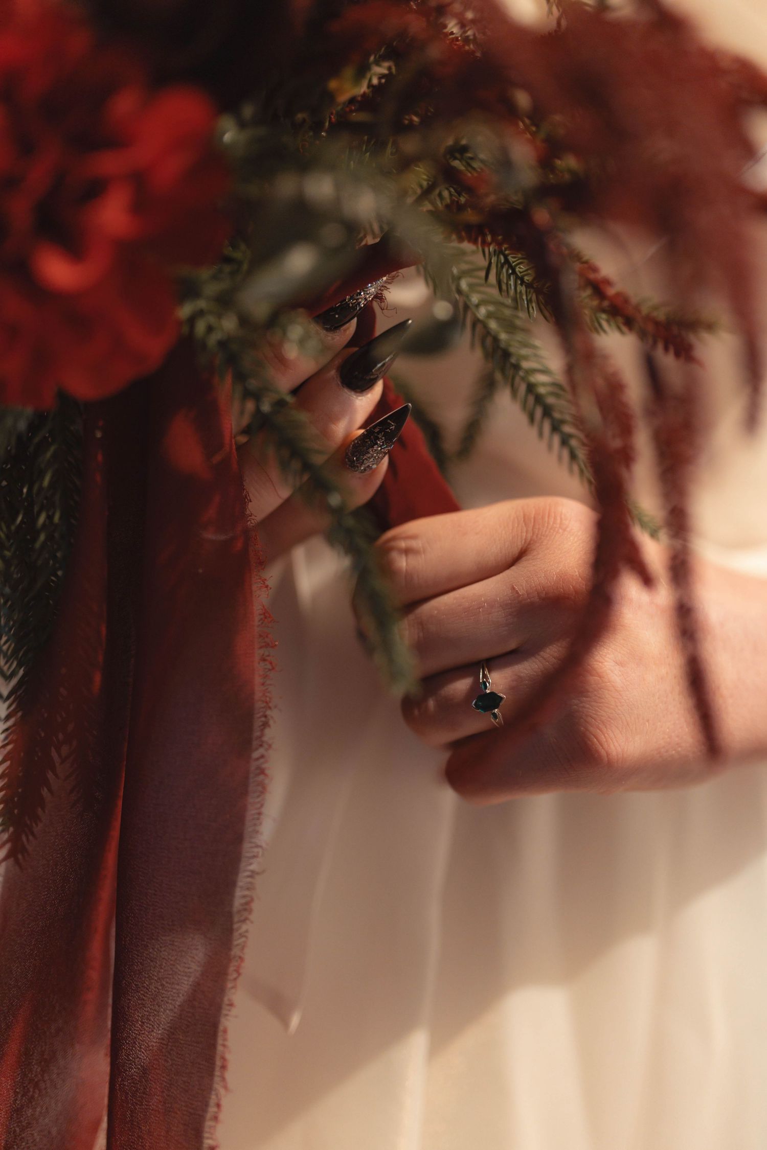 Close-up of bride's hand with dark red nails and sapphire ring holding a lush red floral wedding bouquet.