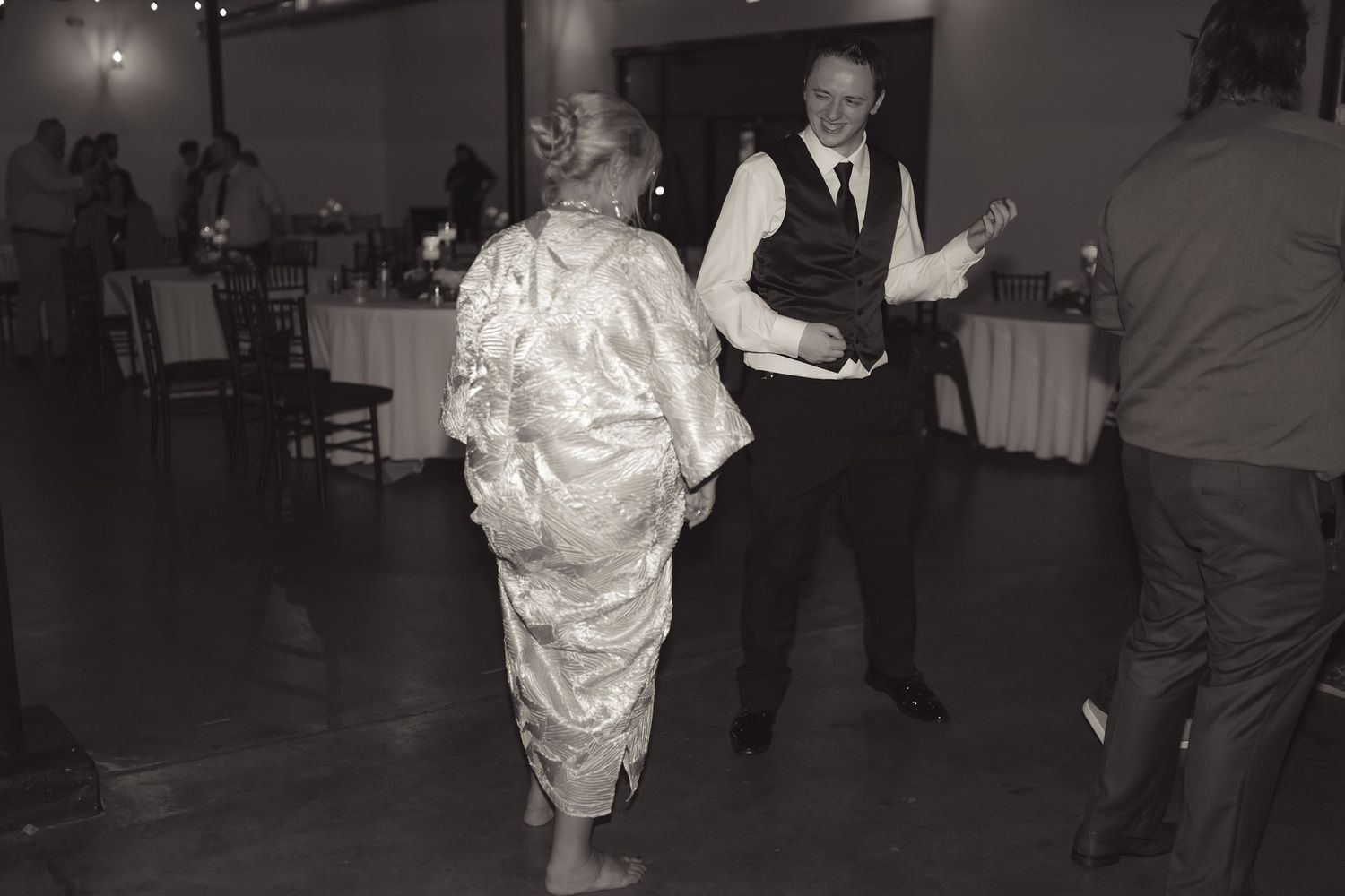 Black and white photo of elderly couple dancing at a wedding reception in a decorated banquet hall.