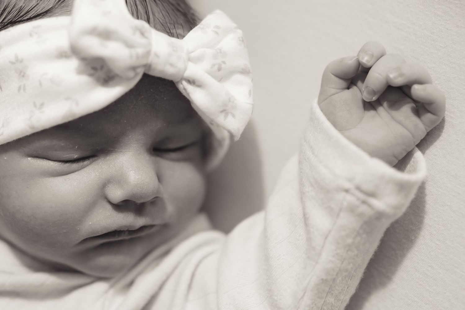 A serene black and white close-up portrait of a sleeping newborn baby wearing a soft bow headband.