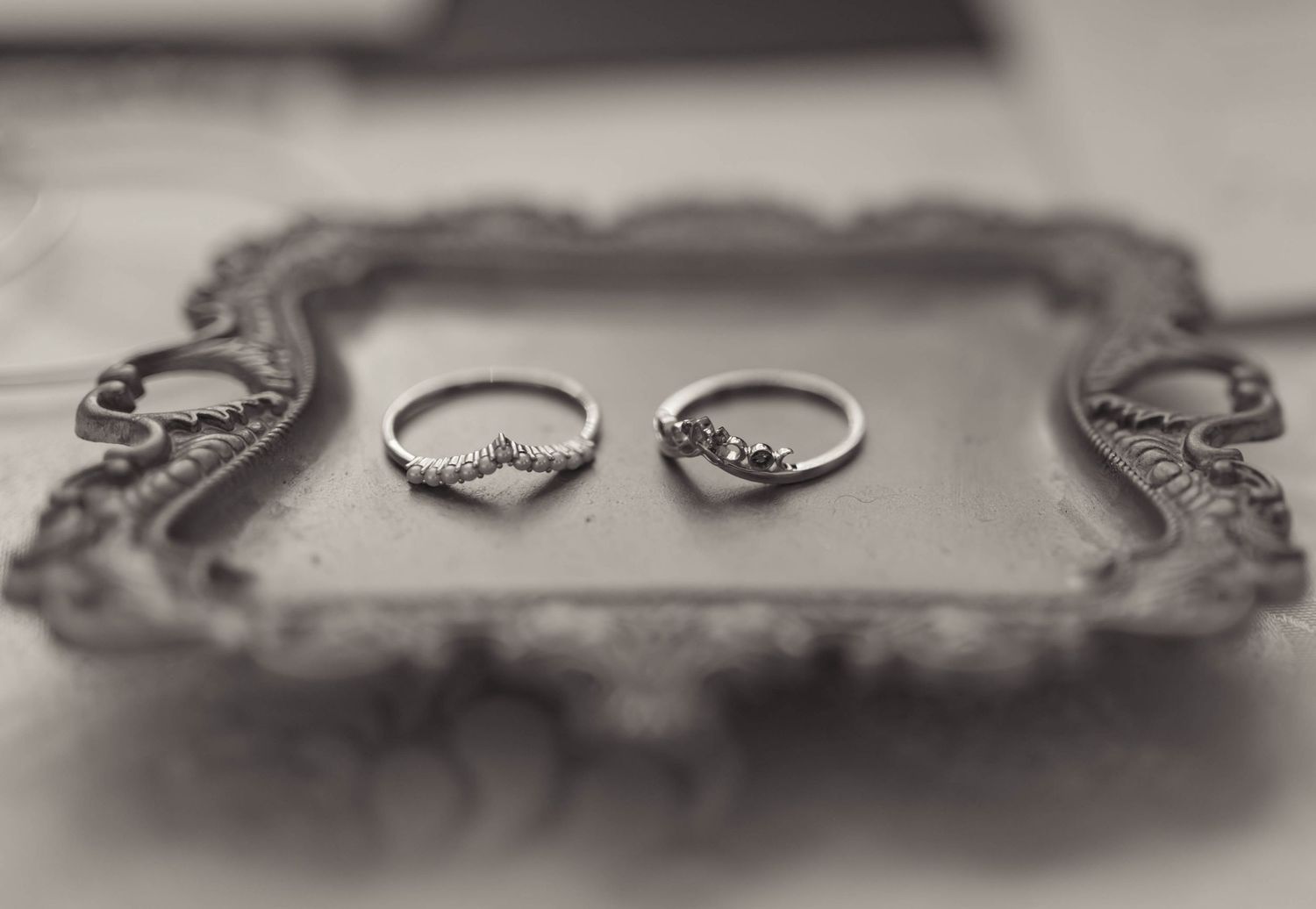 Two delicate silver rings with gemstones displayed on an ornate vintage mirrored tray in black and white.