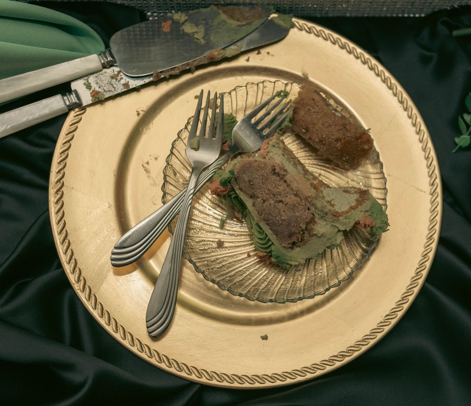 Two slices of wedding cake with green frosting served on a gold charger plate with silver forks.