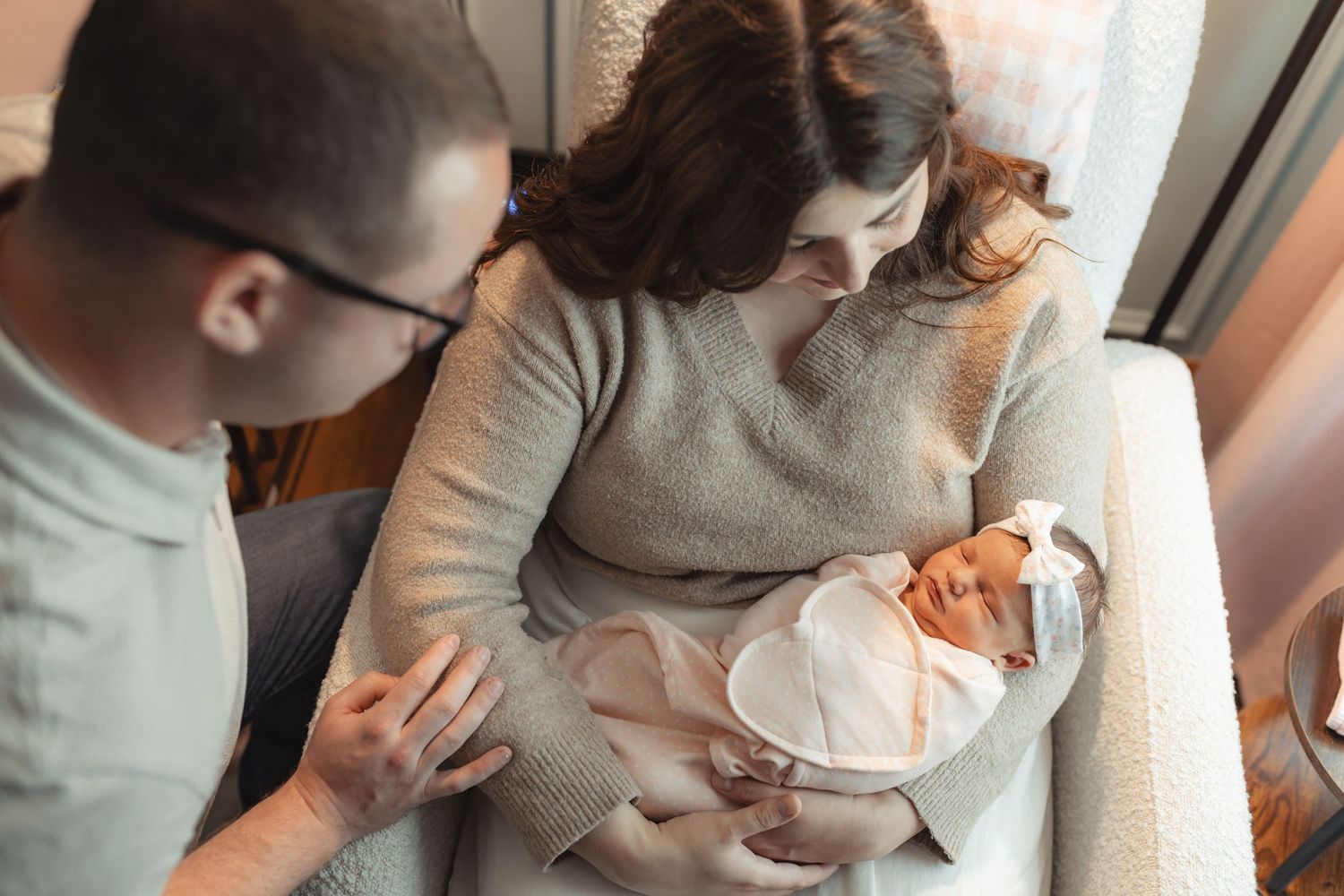 New parents gaze lovingly at their swaddled newborn baby girl during an in-home newborn photography session.