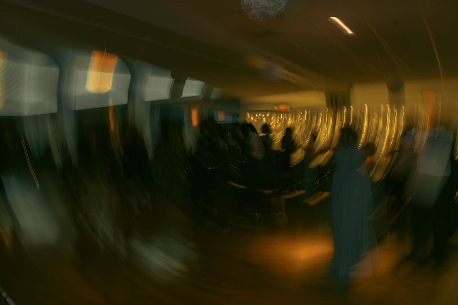 Blurry motion-blur photo of a crowded indoor event with dim lighting and silhouetted figures.