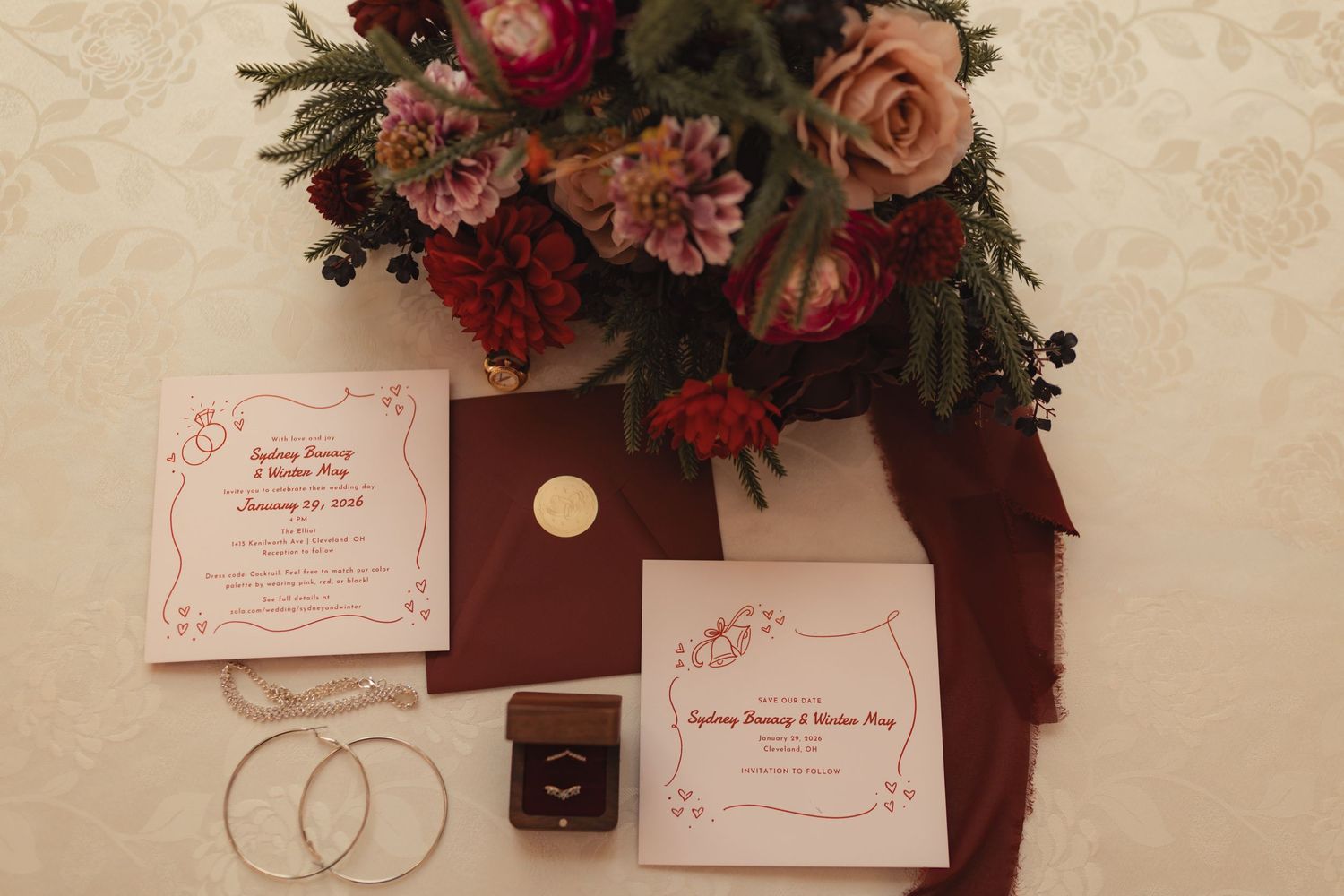 Wedding invitation suite with floral bouquet, gold wax seal envelope, ribbon, and diamond ring box on white background.