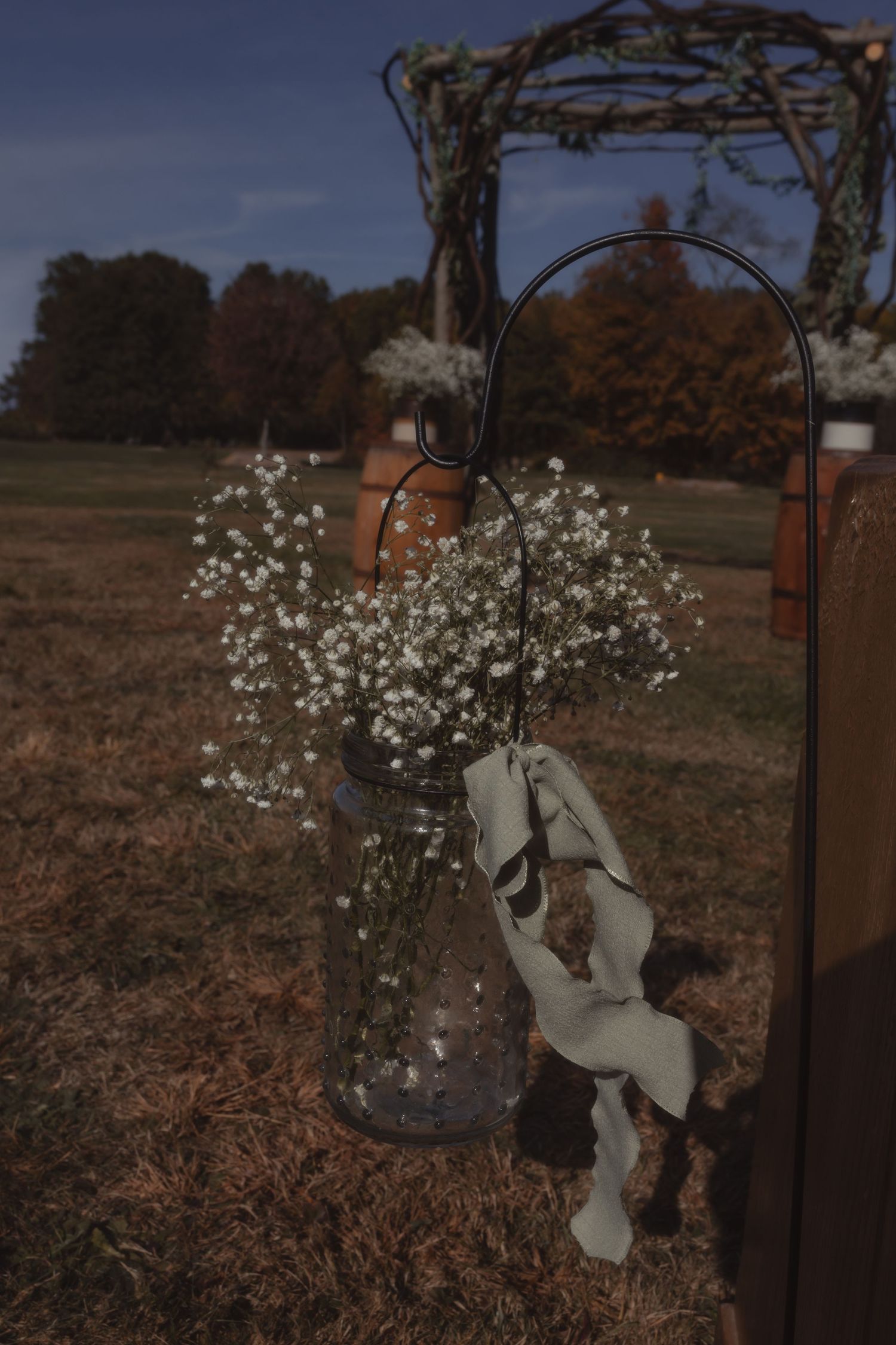 Mason jar with baby's breath flowers hanging on shepherd hook at outdoor fall wedding ceremony.