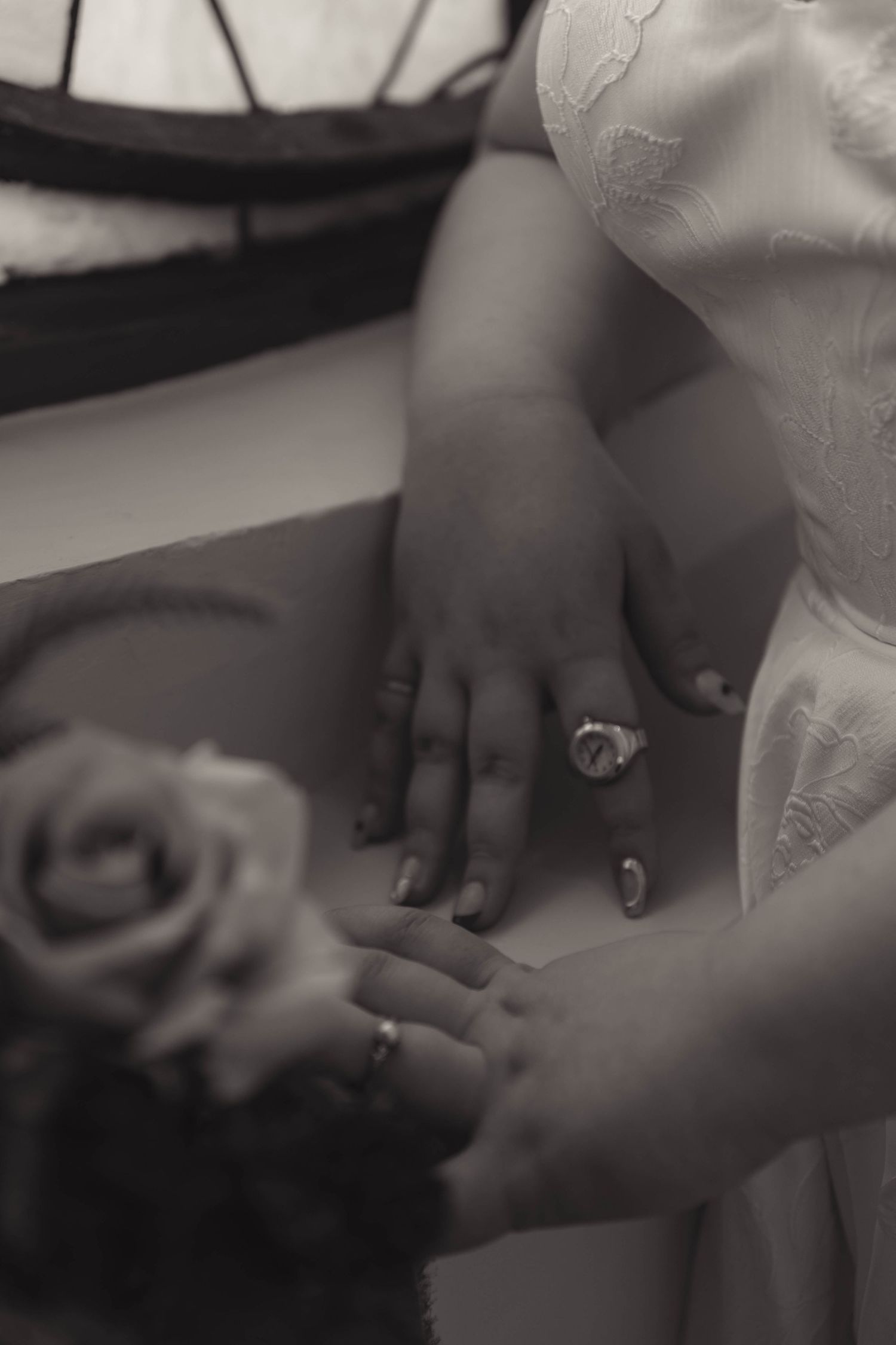 Black and white close-up of two brides hands with rings touching at wedding ceremony.