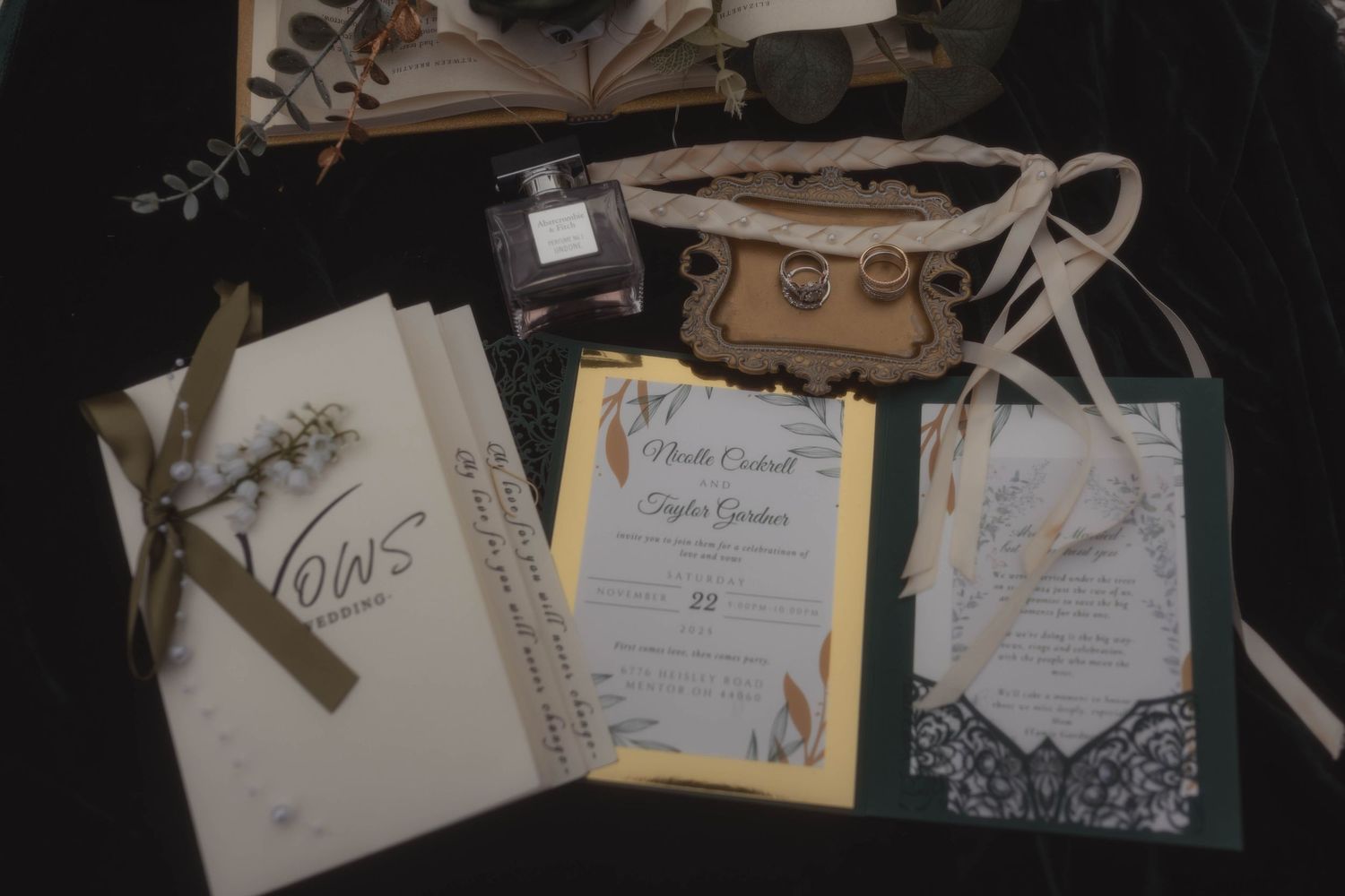 Elegant wedding stationery flat lay featuring vow books, invitations, rings, and decorative accessories on a dark background.