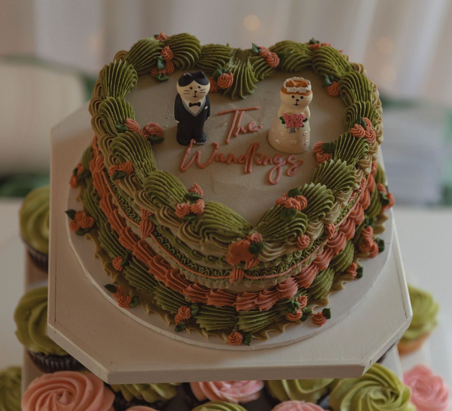 Heart-shaped wedding cake decorated with green and pink frosting, figurines, and The Wangfings inscription.