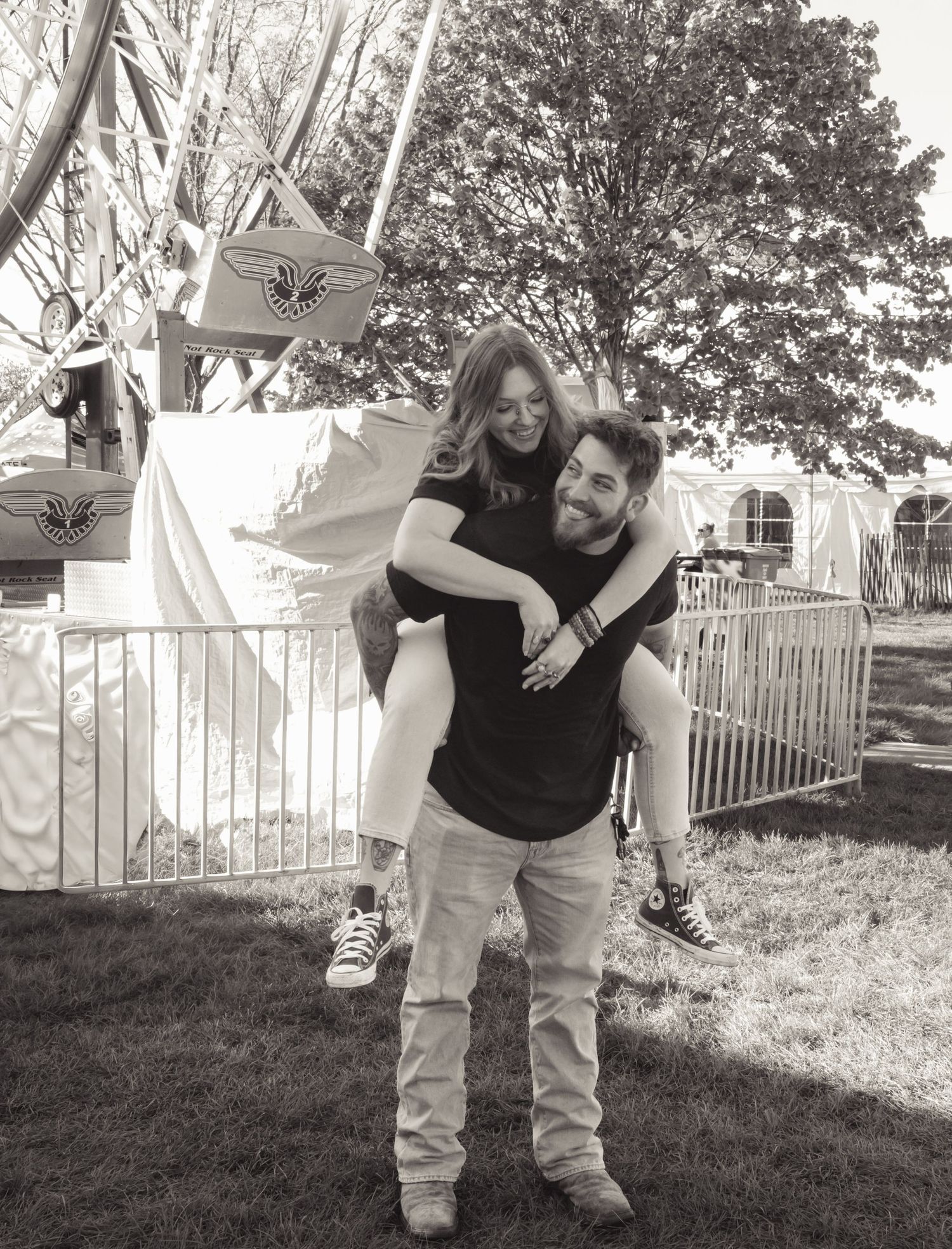 Couple sharing a piggyback ride at a fair, black and white photo with ferris wheel in background.