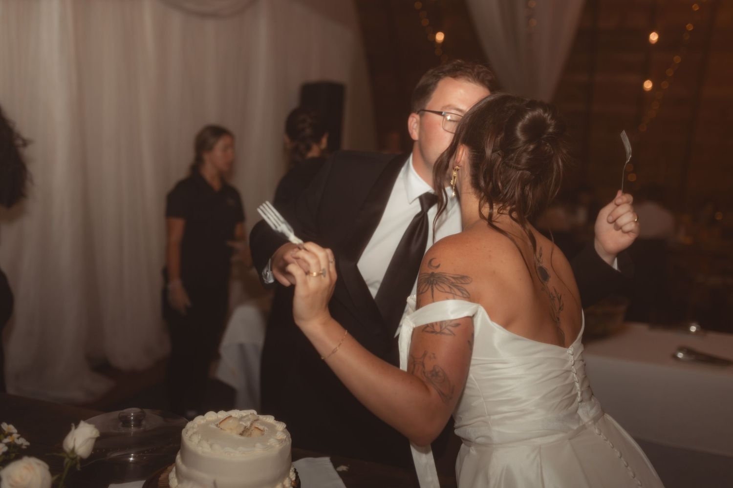 Bride and groom cutting their white wedding cake together at a romantic indoor reception venue.