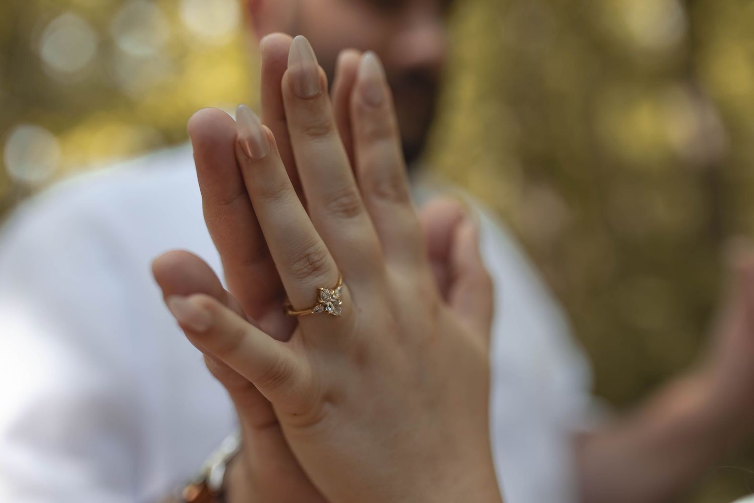 Close-up of a womans hand displaying a beautiful gold engagement ring outdoors.