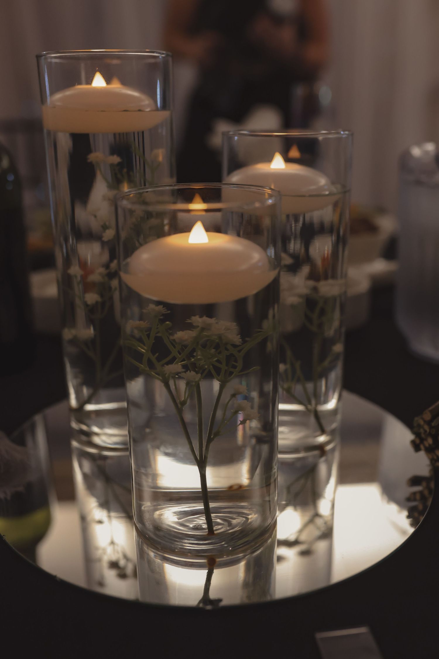Elegant wedding centerpiece with floating candles in glass cylinders on mirror base.