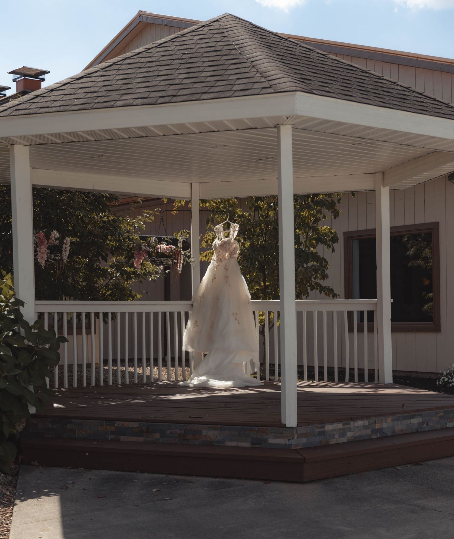 White wedding dress hanging in a gazebo on a sunny day at a rustic venue.