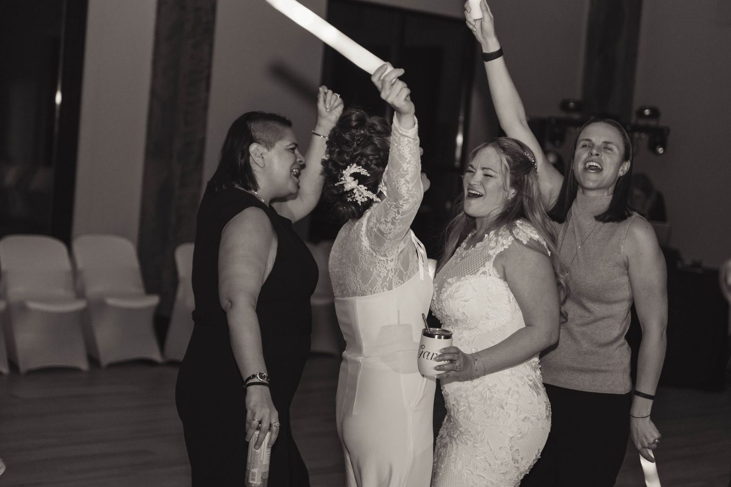Bride and guests dancing joyfully with glow sticks at a wedding reception in black and white photo.