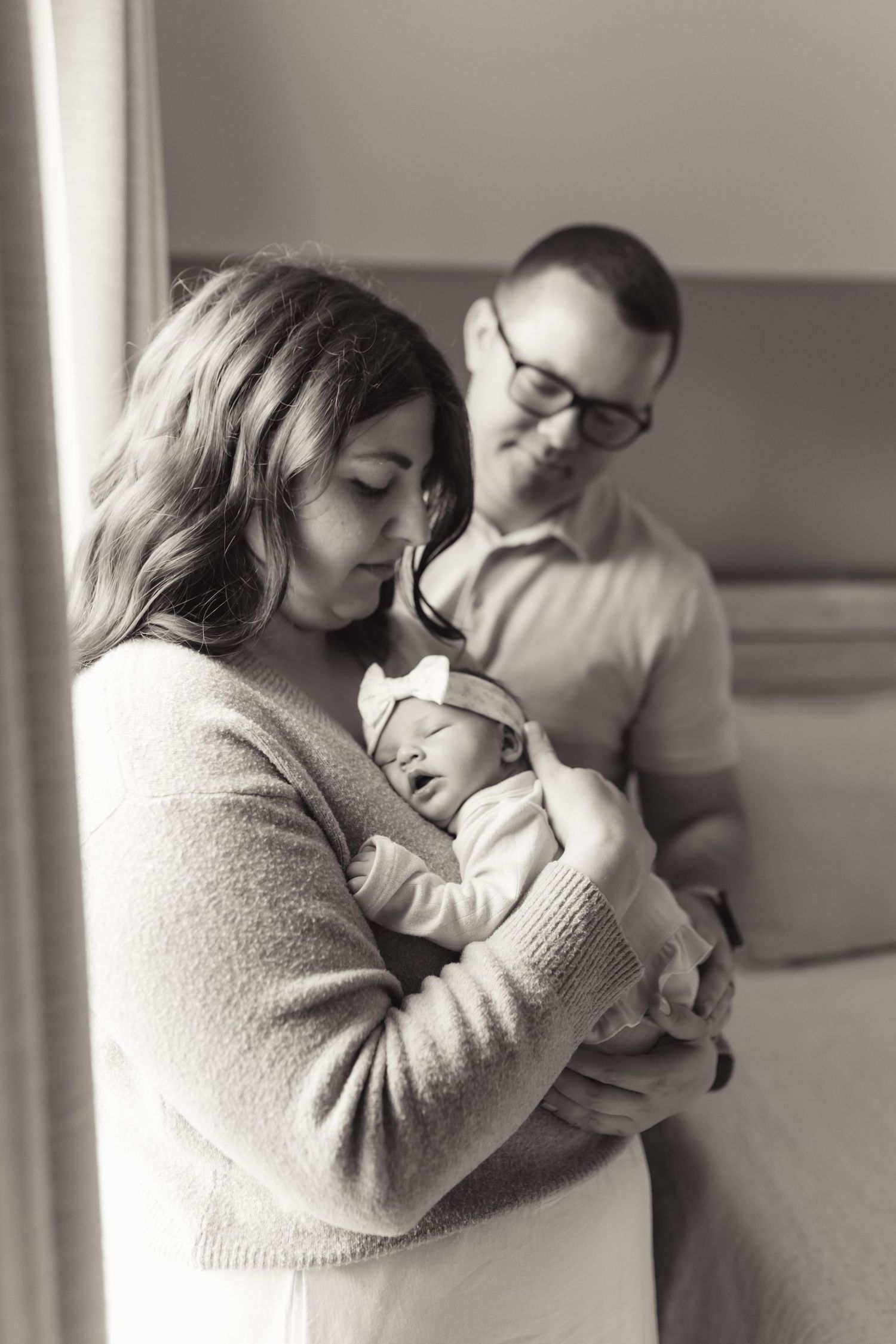 Black and white photo of a mother cradling her newborn baby while father looks on tenderly.