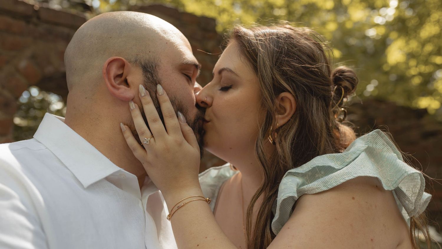 Close-up of a couple sharing a tender kiss outdoors in a lush garden setting during engagement photos.