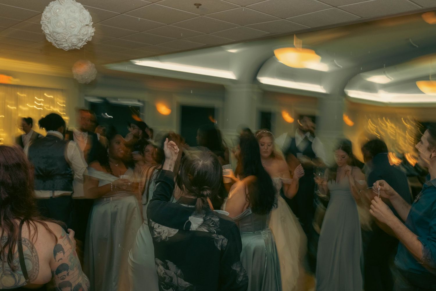 Lively wedding reception dance floor filled with guests celebrating under warm ambient lighting.