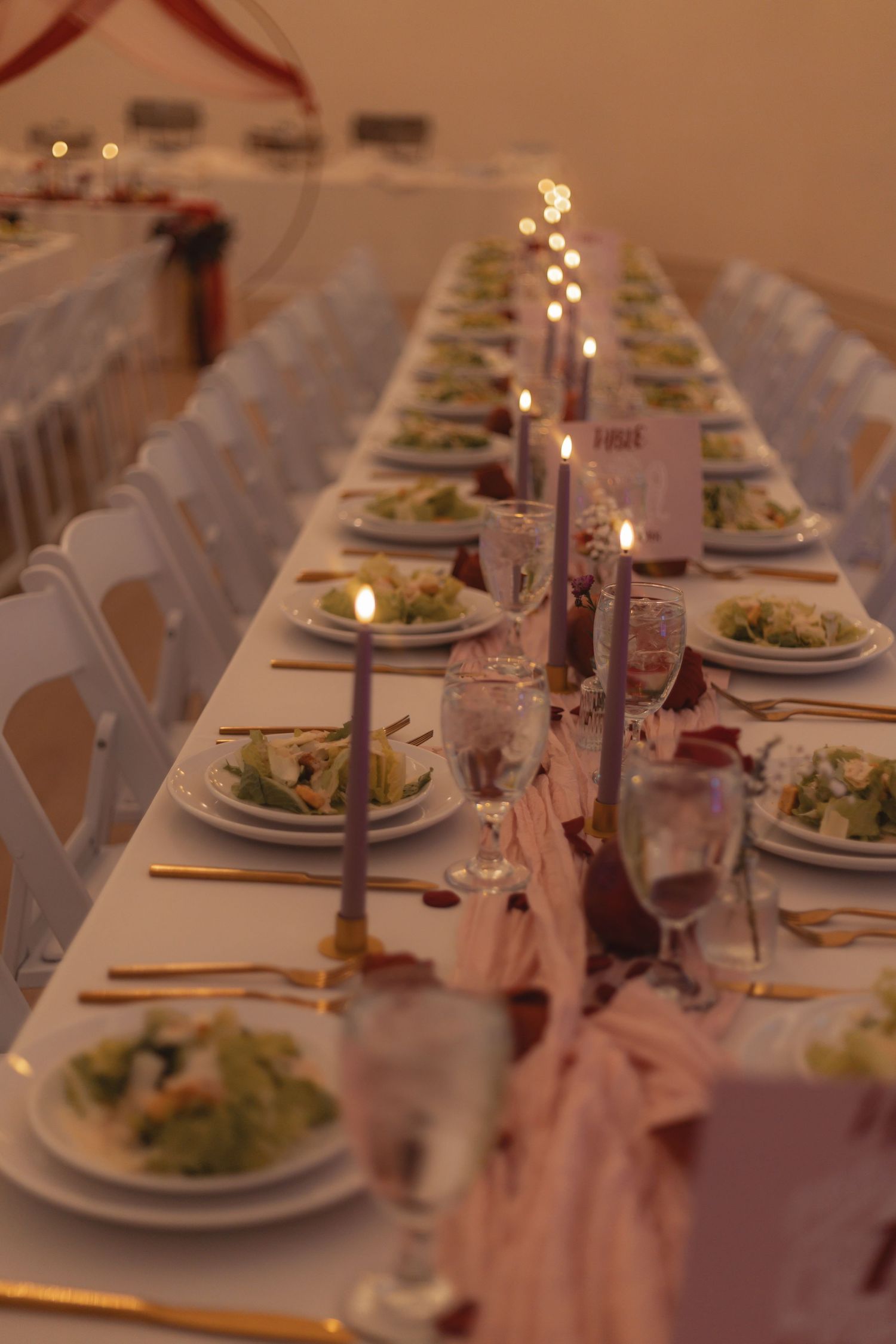 Elegant wedding reception table set with lavender candles, gold cutlery, salad plates, and pink runner decor.