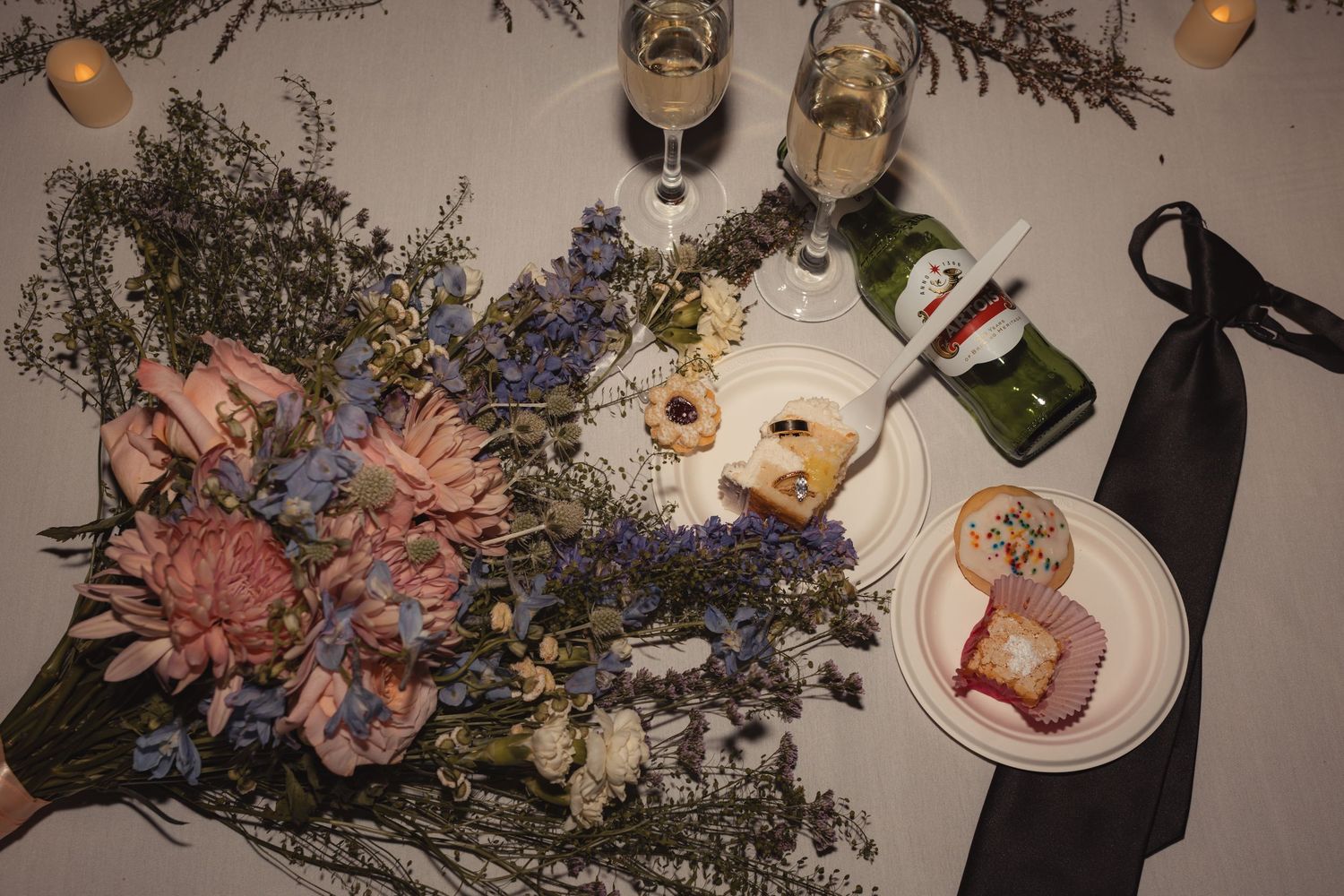 Elegant wedding table with floral bouquet, champagne glasses, appetizers, and a black tie on white linen.
