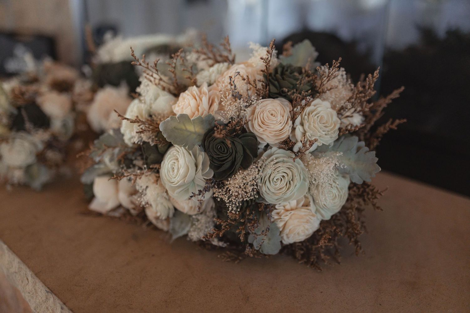 Rustic wedding bouquets with cream sola wood roses, eucalyptus, and dried wildflowers arranged on a wooden table.
