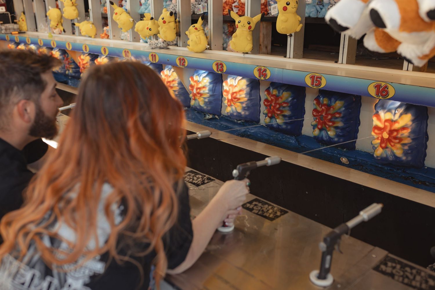 Couple playing a duck shooting carnival game with stuffed animal prizes at a fair.