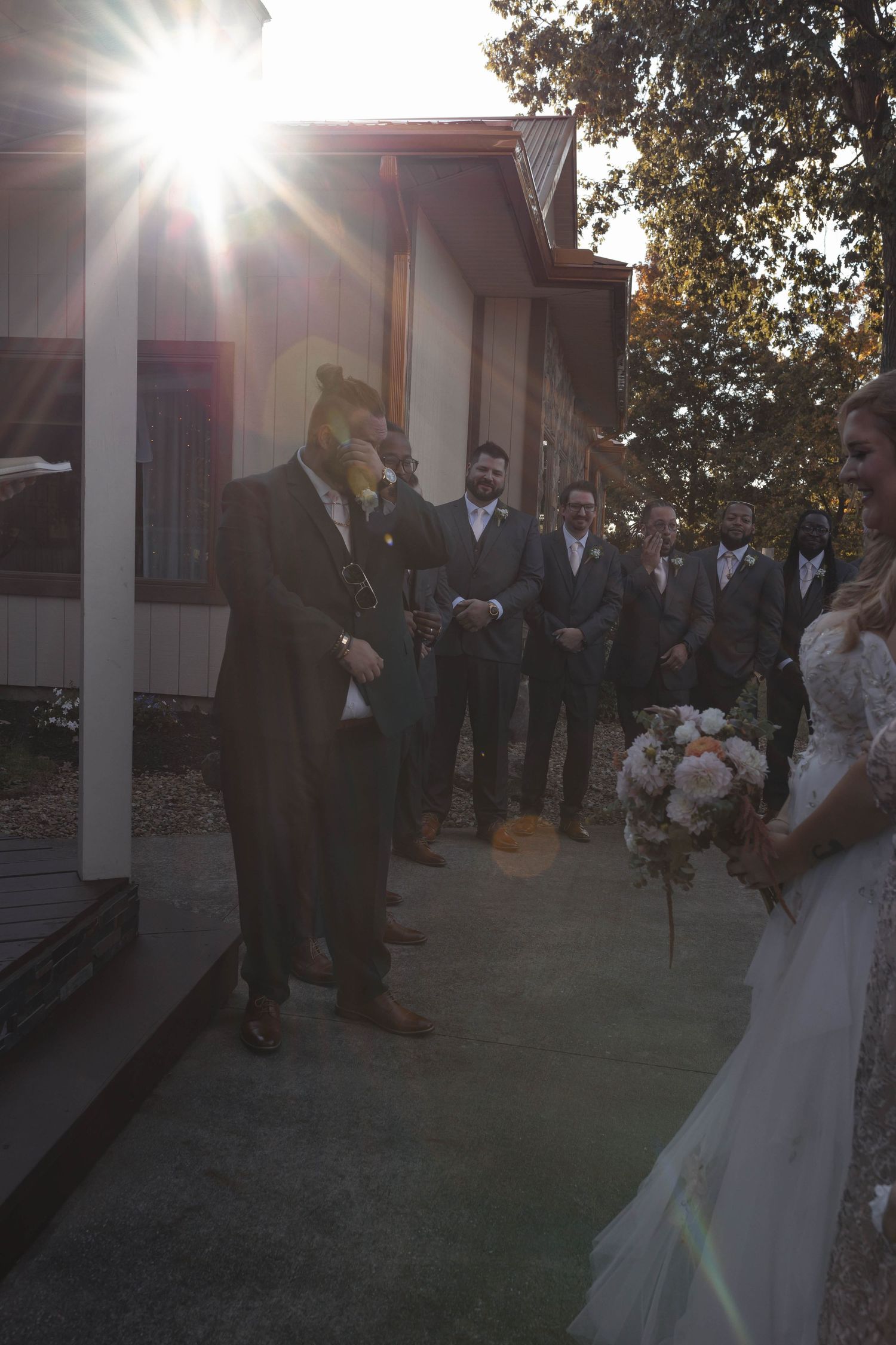 Groom reacts emotionally as bride approaches during outdoor wedding ceremony with groomsmen watching.