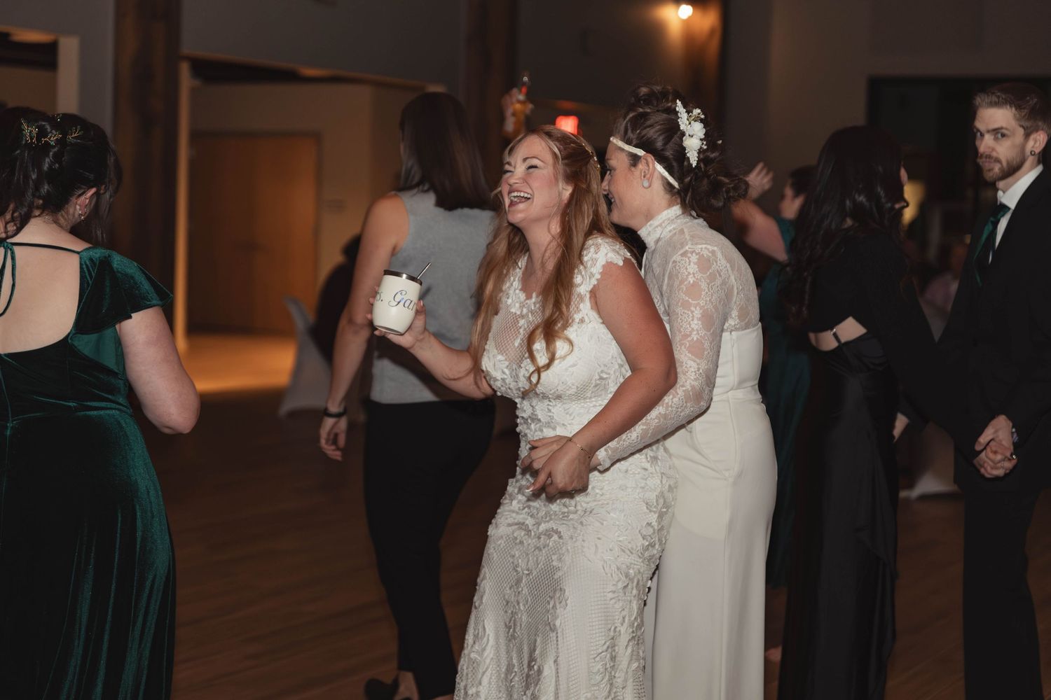 Two brides in white lace gowns dancing joyfully together at their wedding reception.