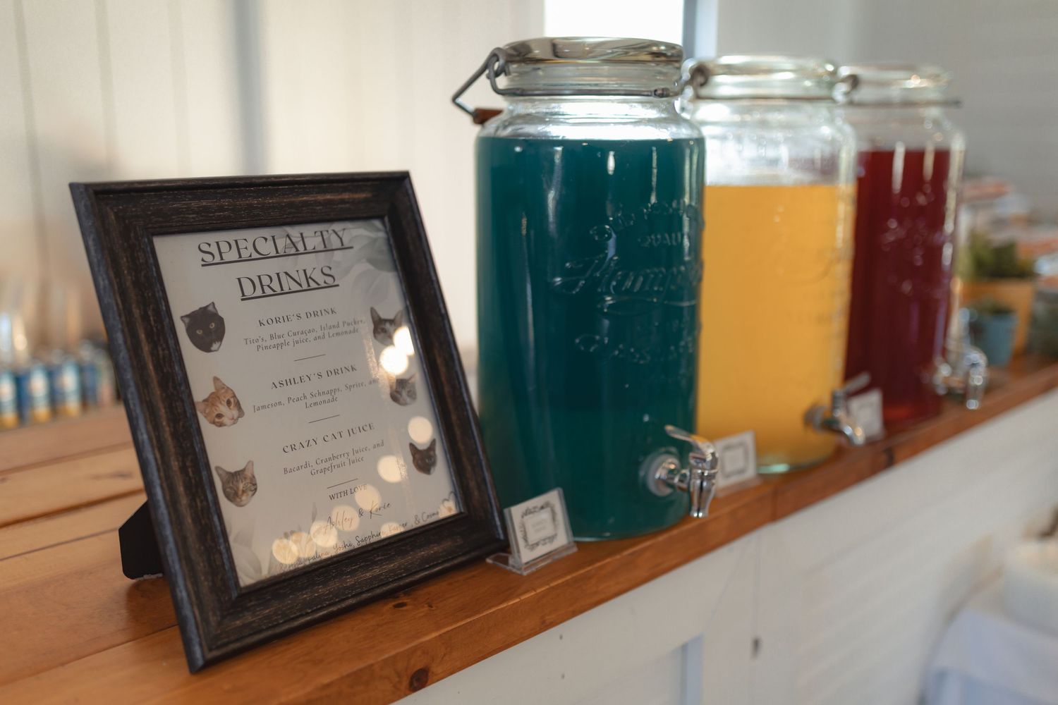 Wedding specialty drinks station with colorful beverages in glass dispensers on rustic wooden shelf.