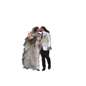 A bride and groom share a kiss, she holds a floral bouquet in a lace gown, he wears a white tuxedo jacket.