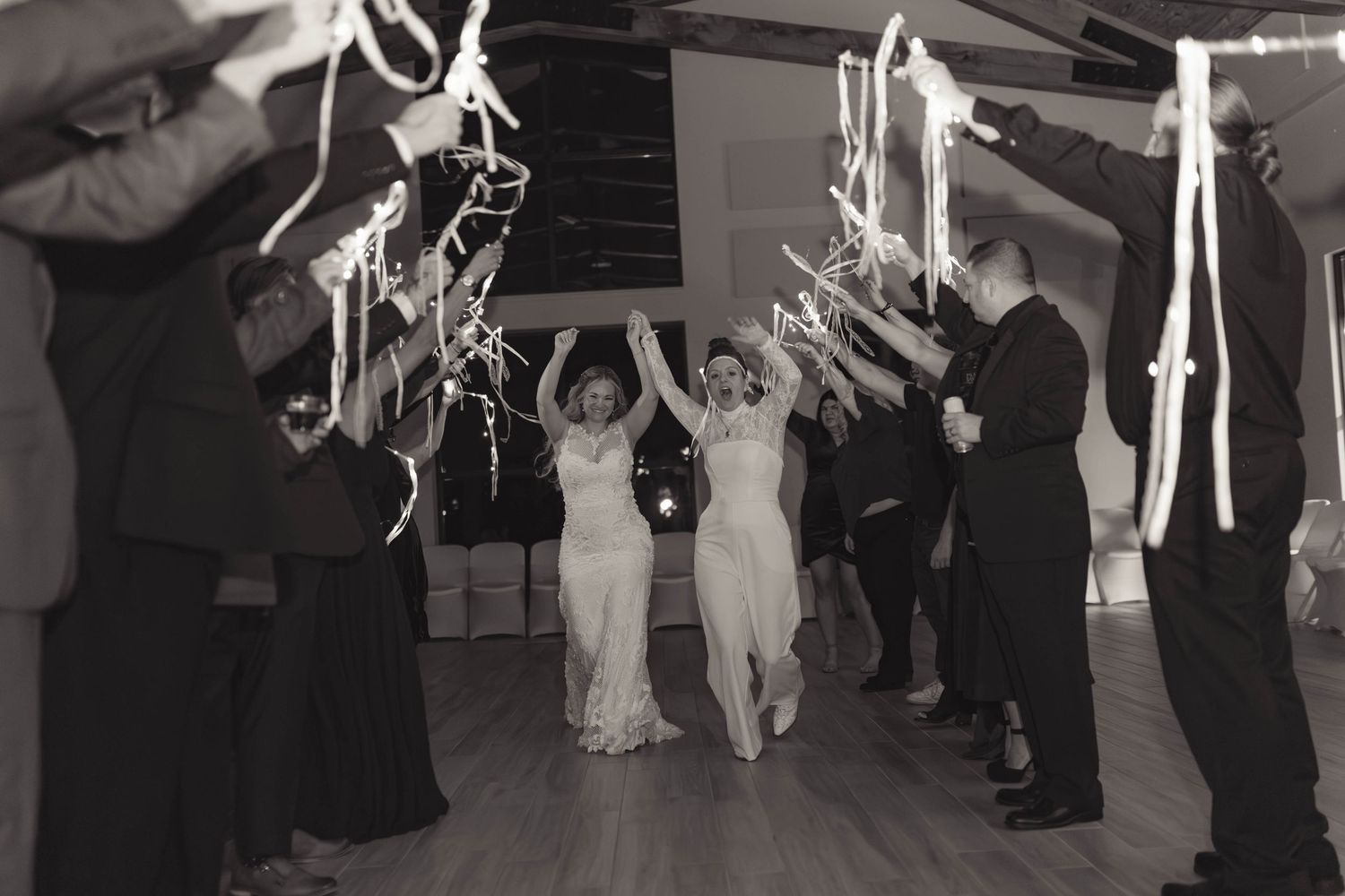 Two brides exit through a sparkler tunnel during their wedding reception celebration.