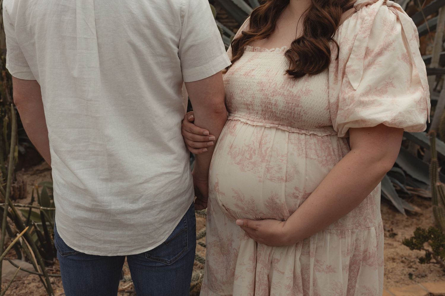 Pregnant woman in floral dress holding baby bump beside partner outdoors during maternity photo session.