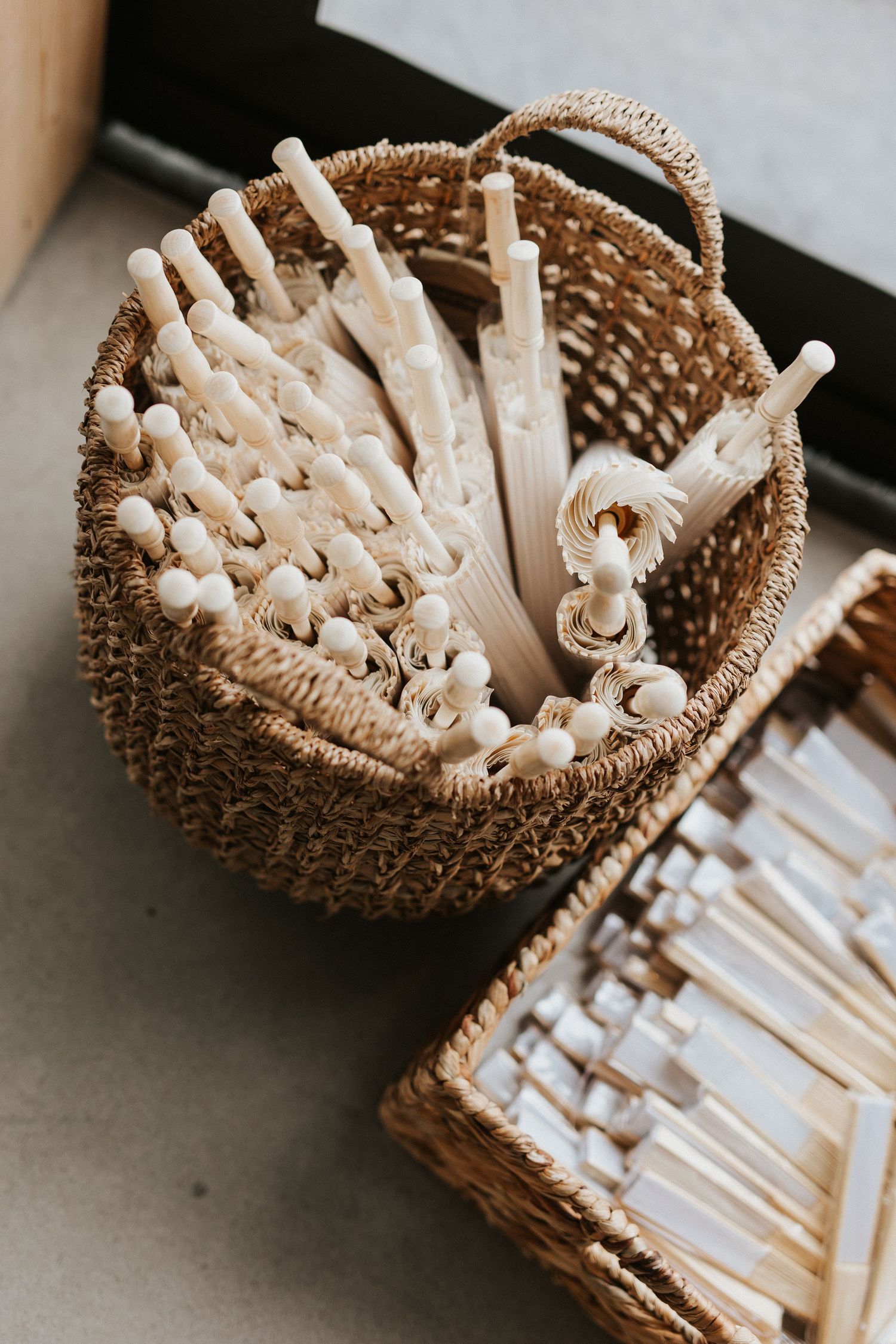 White paper parasols neatly arranged in woven baskets for an outdoor wedding event.
