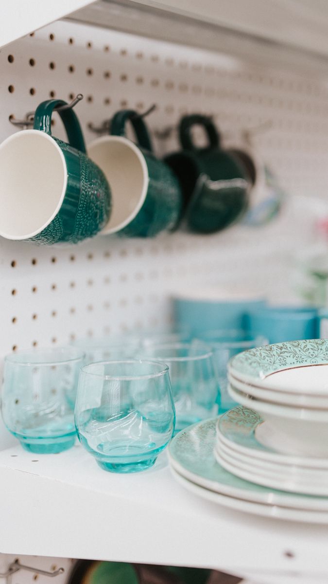 Turquoise glassware and white plates arranged on pegboard shelving.