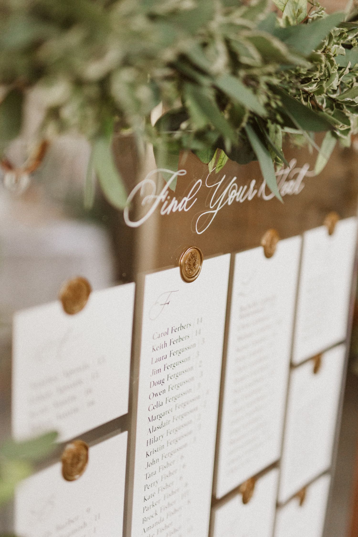 Wedding seating chart with wax seals and elegant calligraphy under greenery.