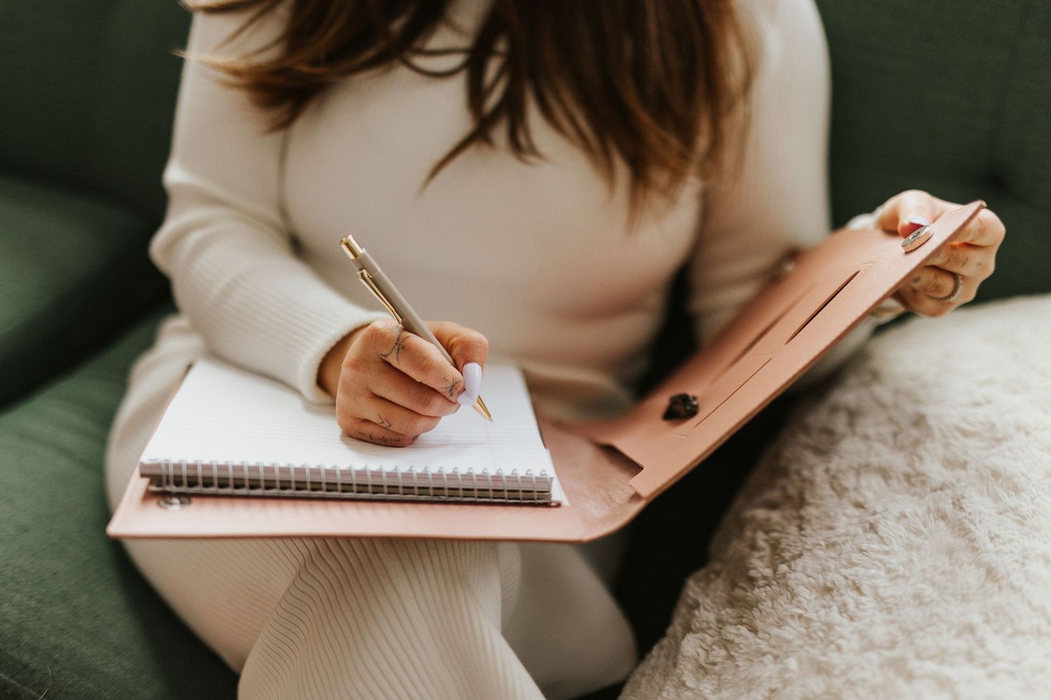 Close-up of hands writing in a notebook while sitting on a cozy couch.