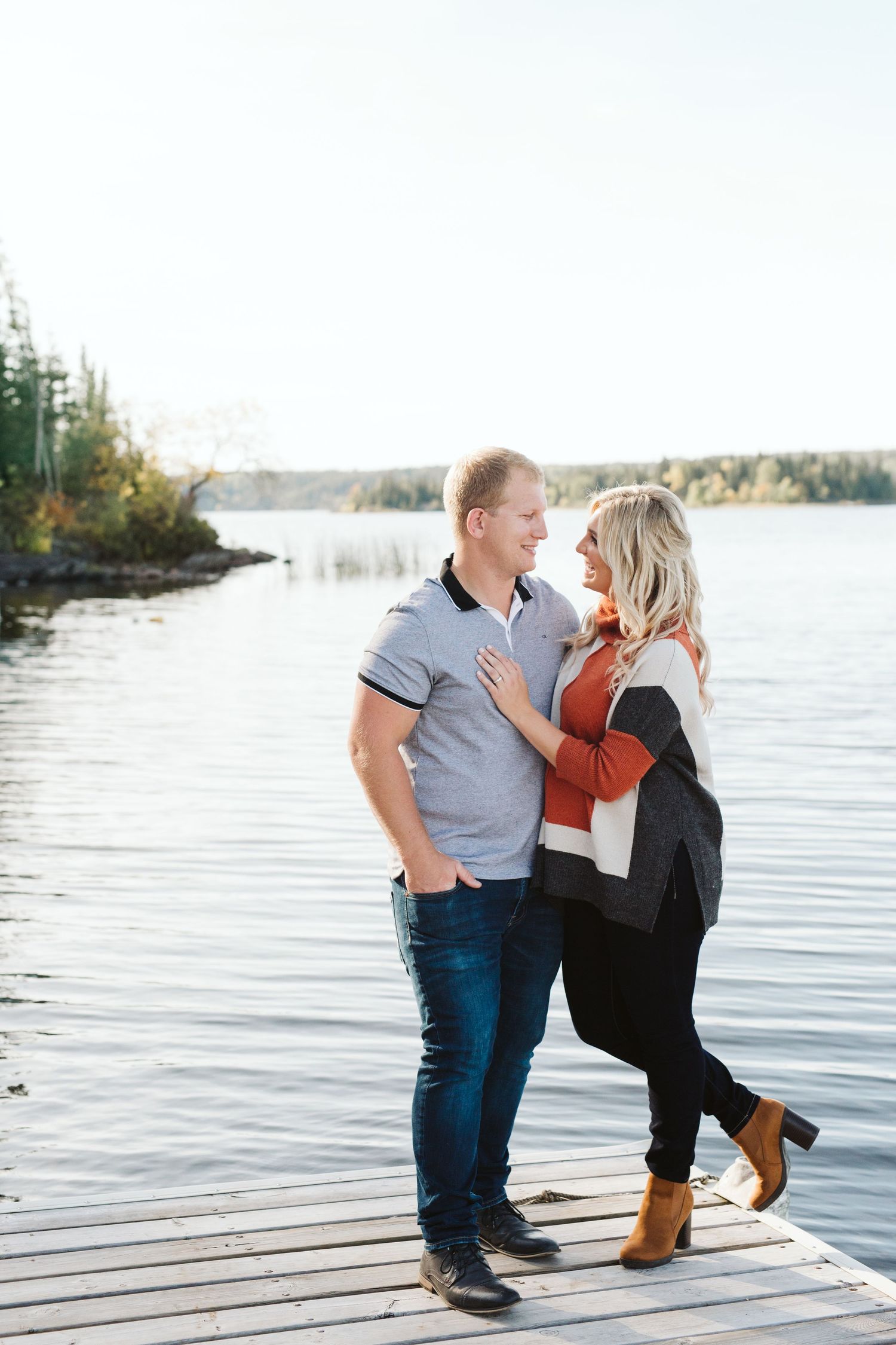 A couple shares an intimate moment while sitting on a wooden dock by a serene lake.
