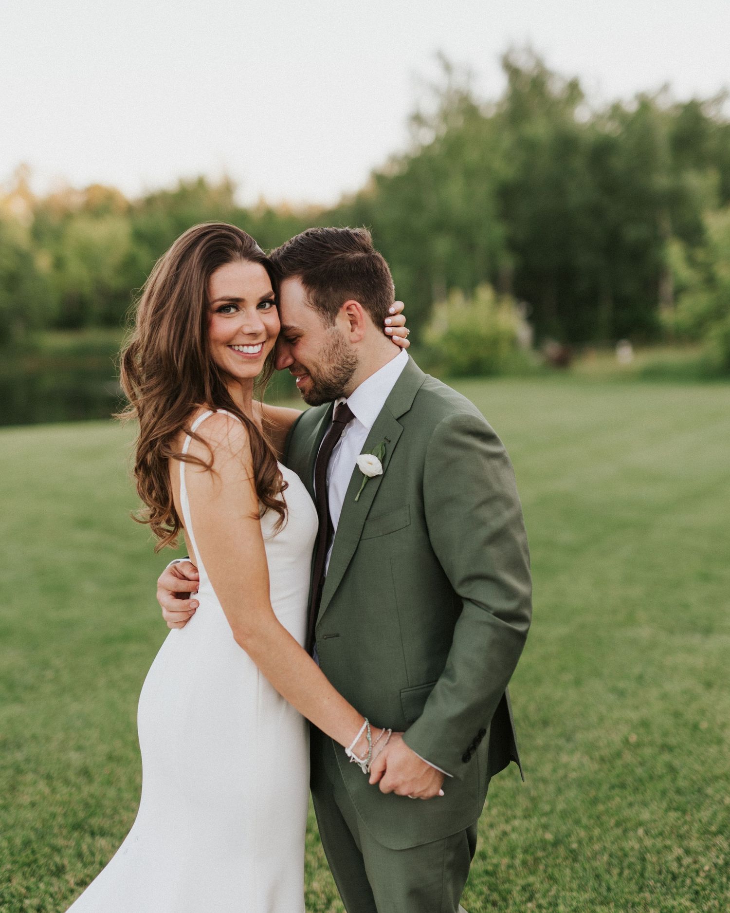 Intimate wedding portraits in a green field with bride in white dress and groom in olive suit.