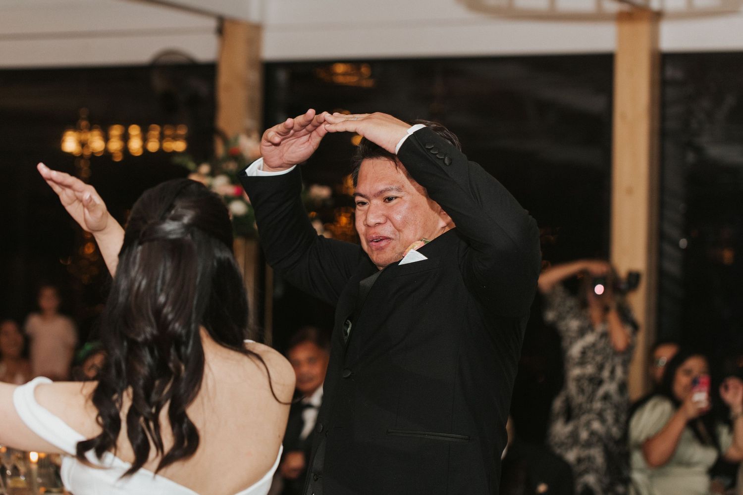 Wedding guests dancing and celebrating together on a dimly lit dance floor at an evening reception.