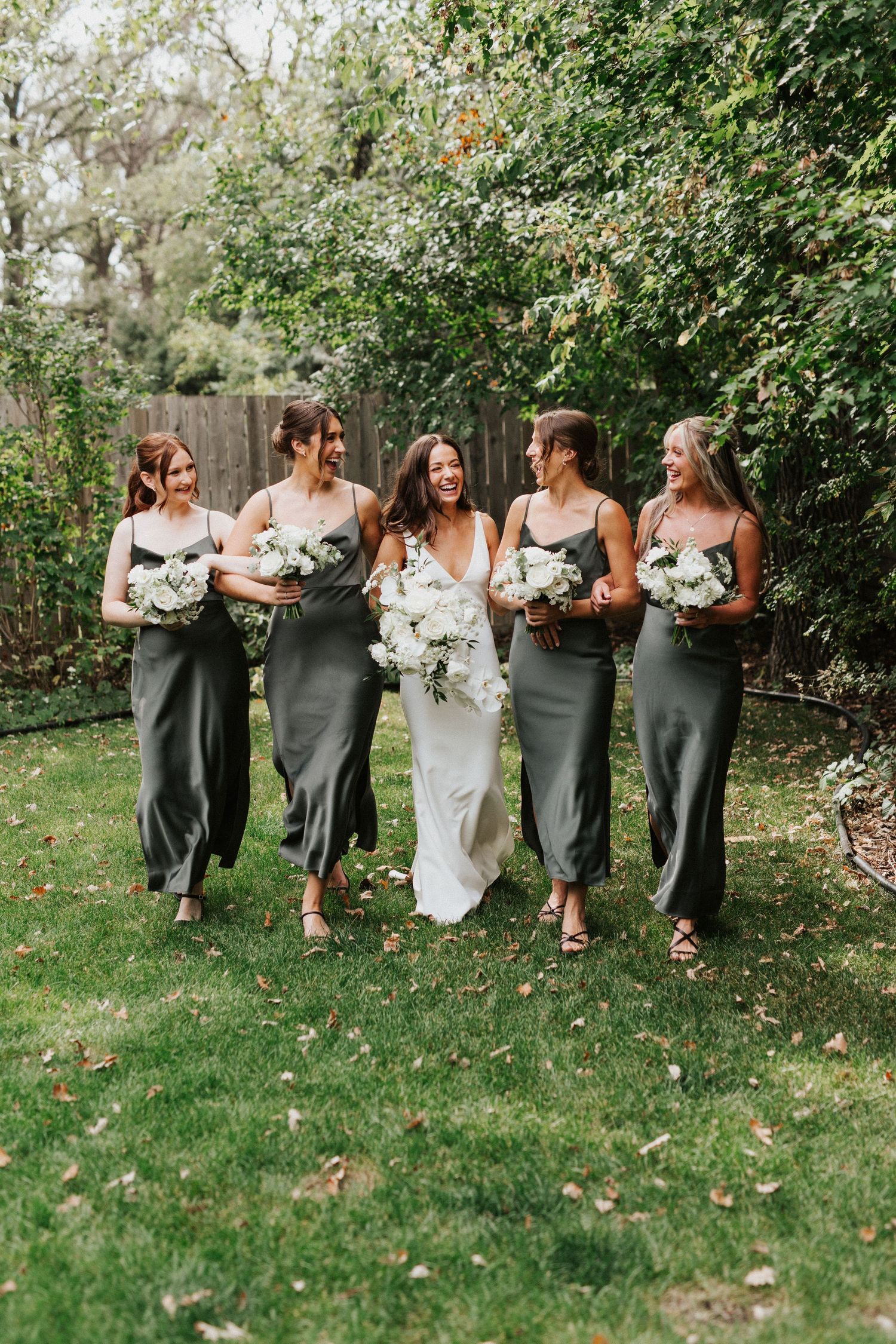 Manitoba Wedding Photographer. Wedding party walks together on grass with bridesmaids wearing coordinating grey dresses.