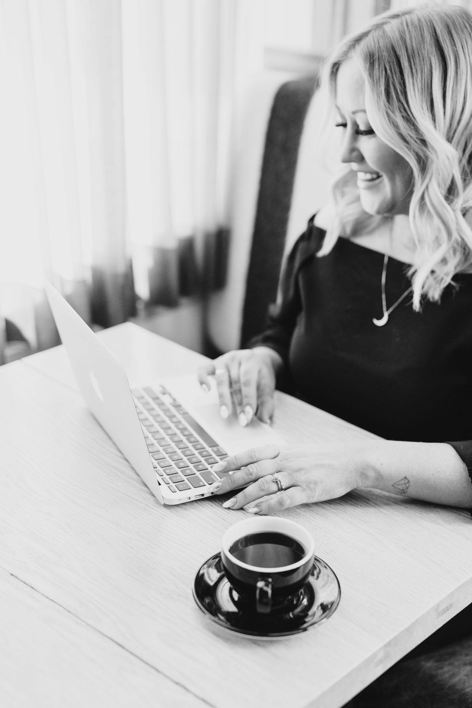 Black and white image of coffee cup and laptop on minimalist workspace.