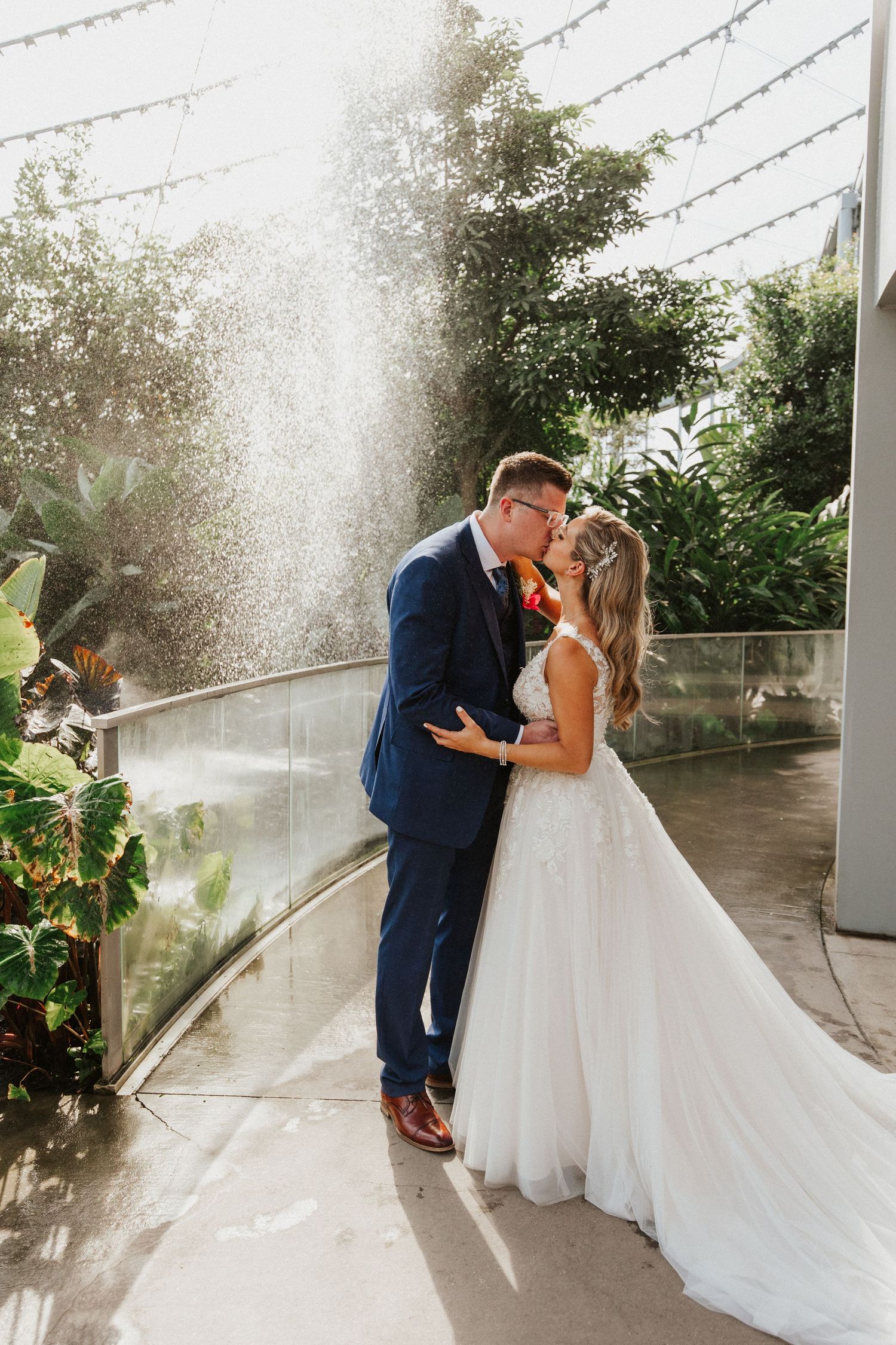 Wedding couple shares romantic kisses in a bright sunlit venue with decorative string lights.