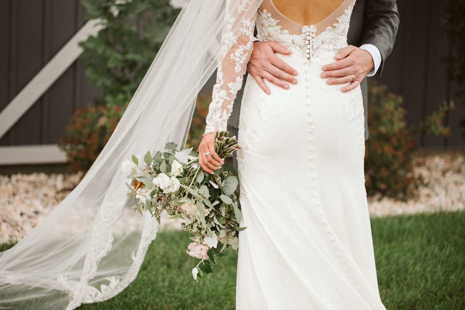 Close-up of lace wedding dress with flowing veil and delicate floral bouquet.