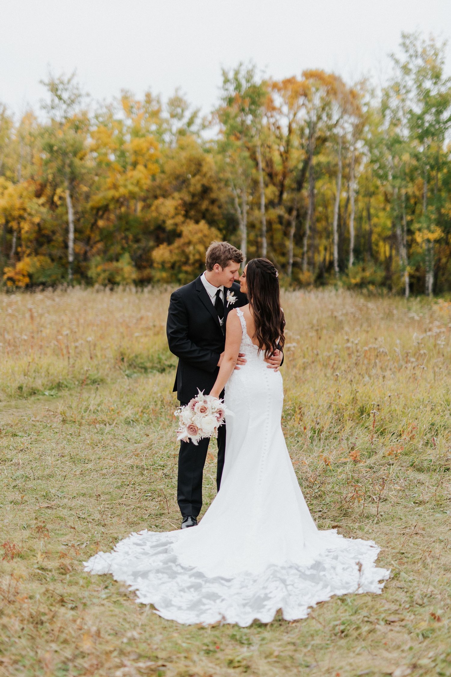 Wedding couple shares intimate moments in an autumn field with golden trees.