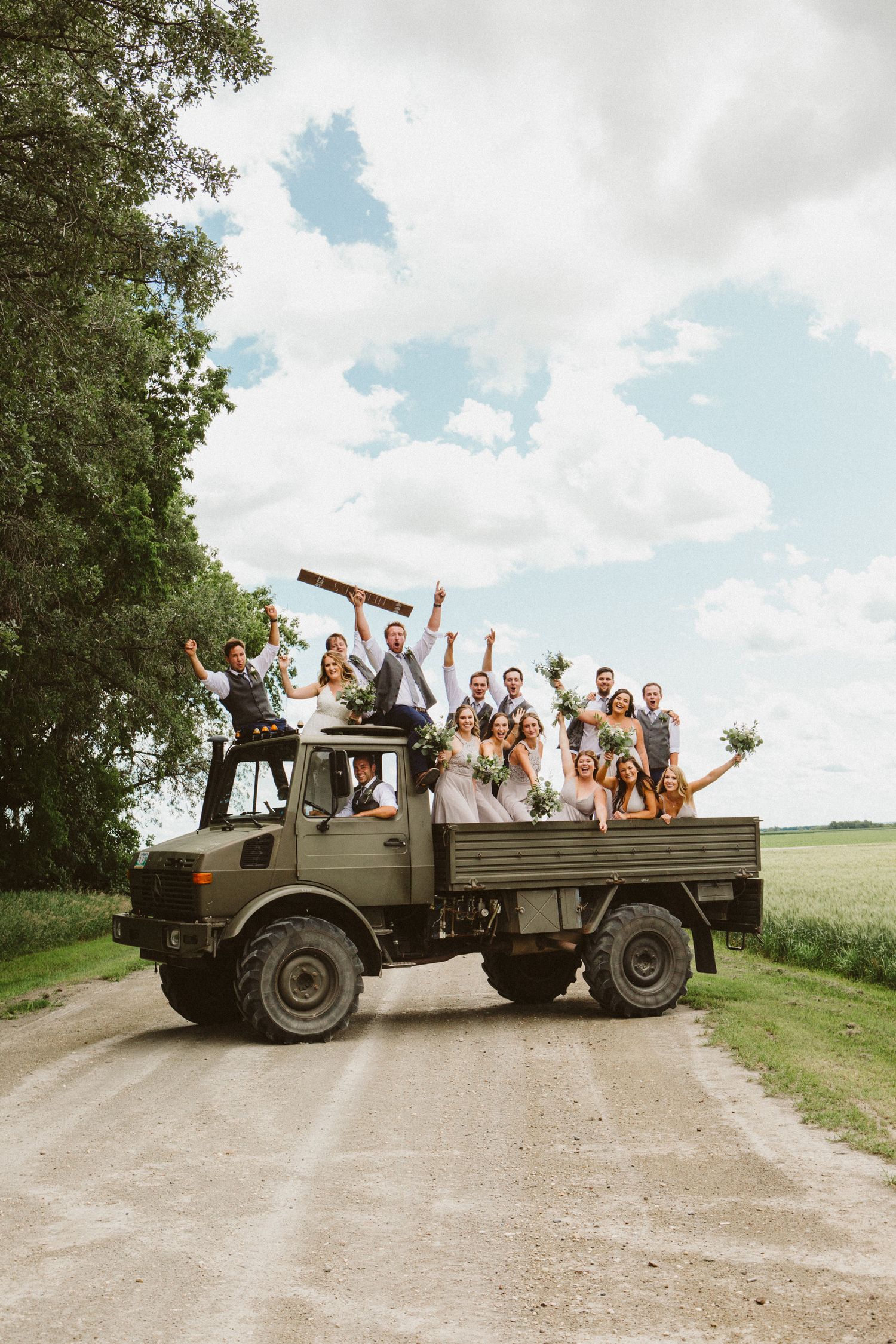 Wedding party riding in vintage military truck on country road celebrating.